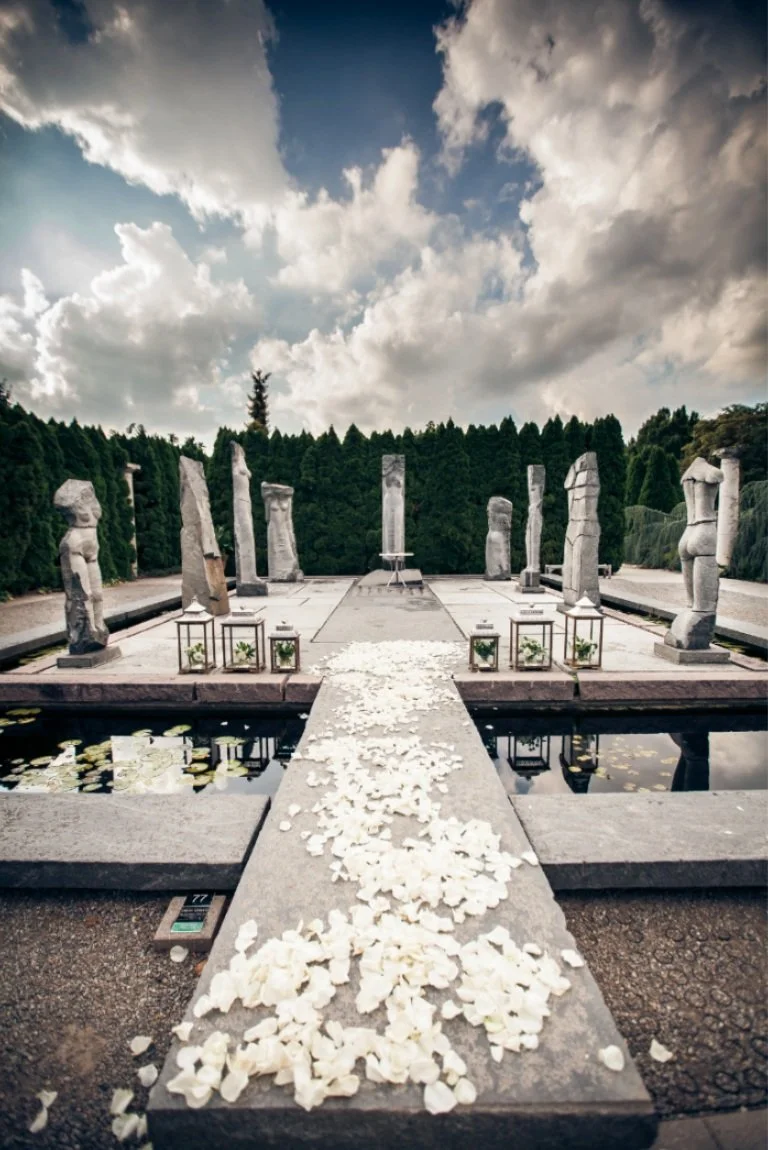 A wide shot of an outdoor ceremony site adorned with white flower petals and stone statues.