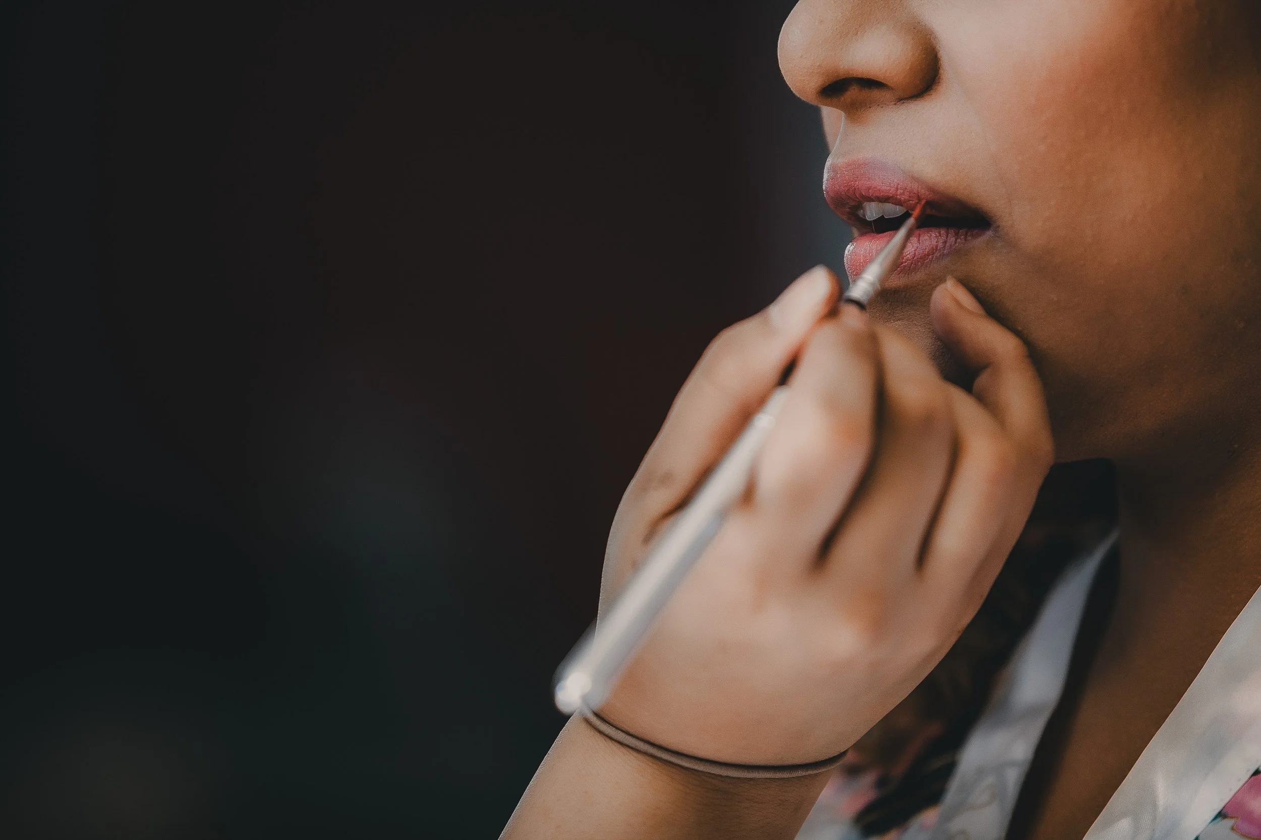 Close-up of a woman applying pink lipstick with a small brush.