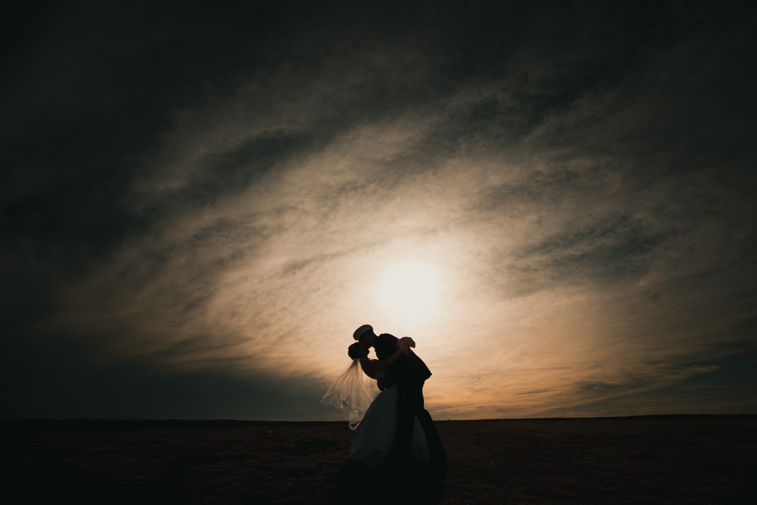 Silhouette of a couple kissing at sunset with a cloudy sky.