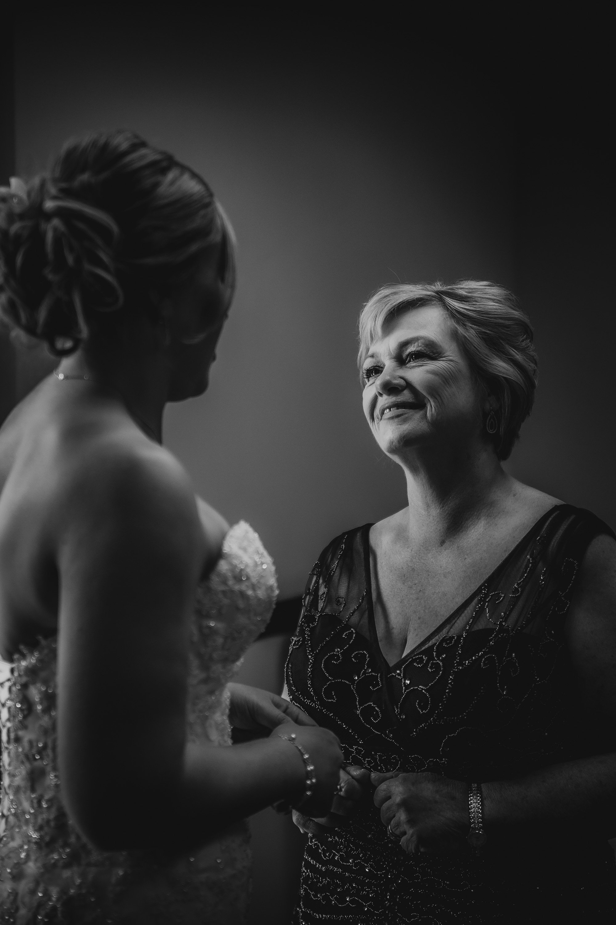 A woman in a wedding dress smiling at an older woman in a black dress.
