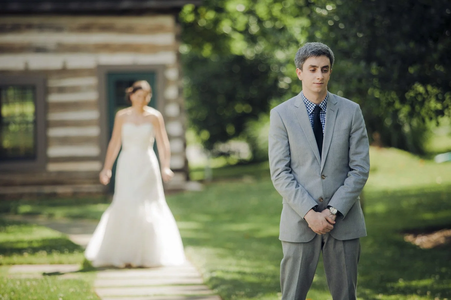A groom stands while the bride walks up to him from behind during their first look.