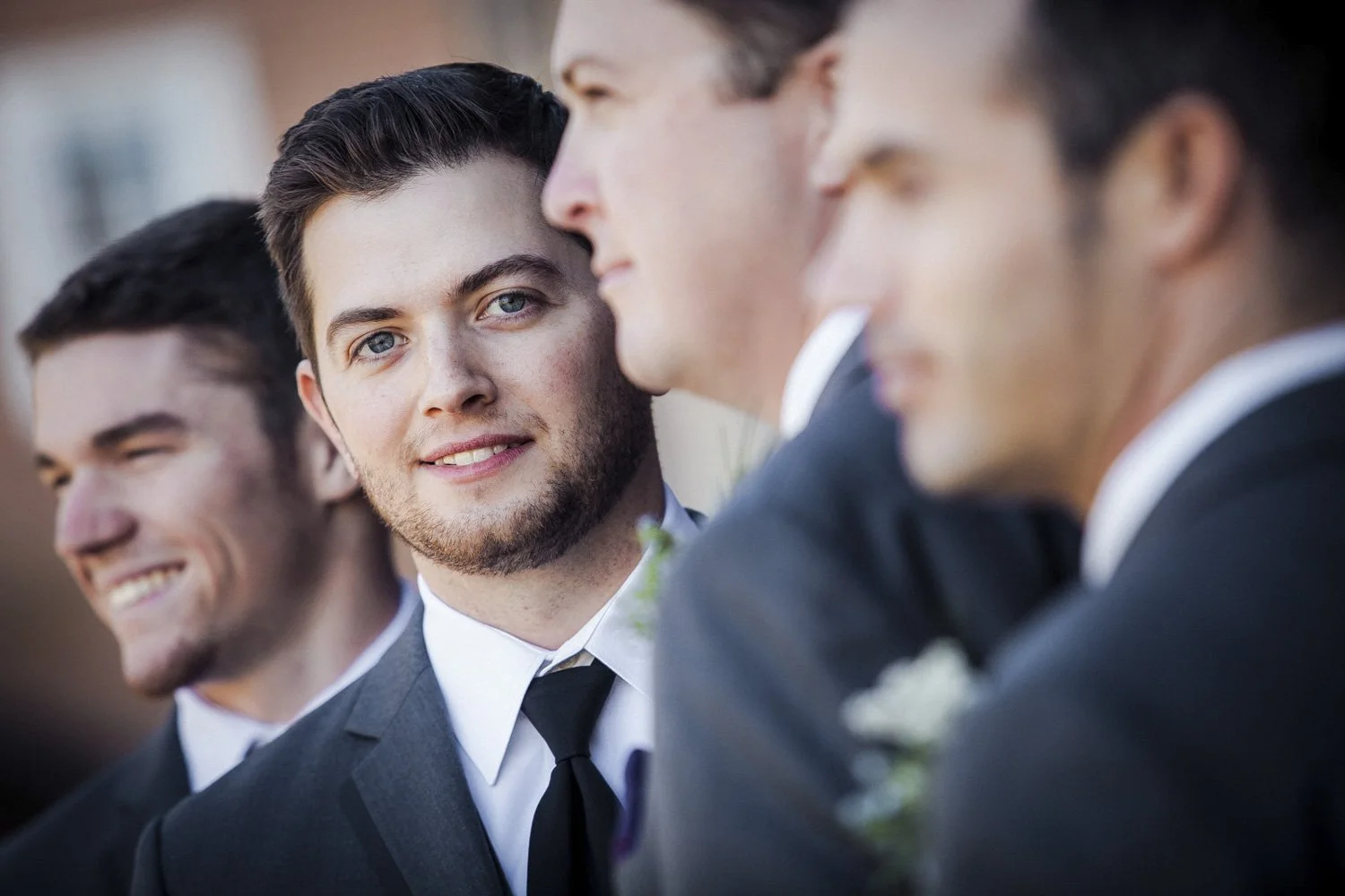 A groom smiles at the camera while posing with his 3 groomsmen.