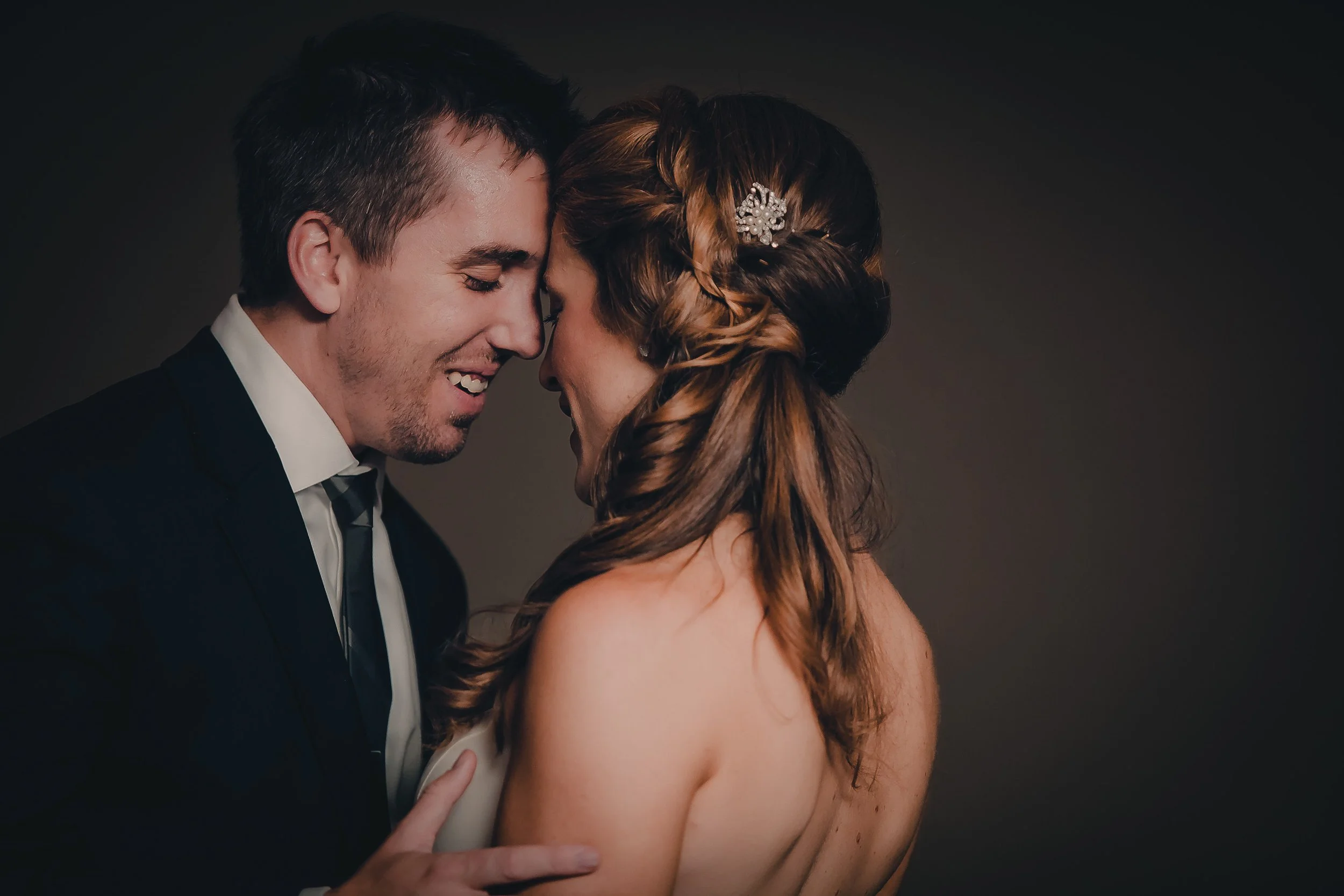 A couple on their wedding day, with foreheads touching, smiling, and embracing.