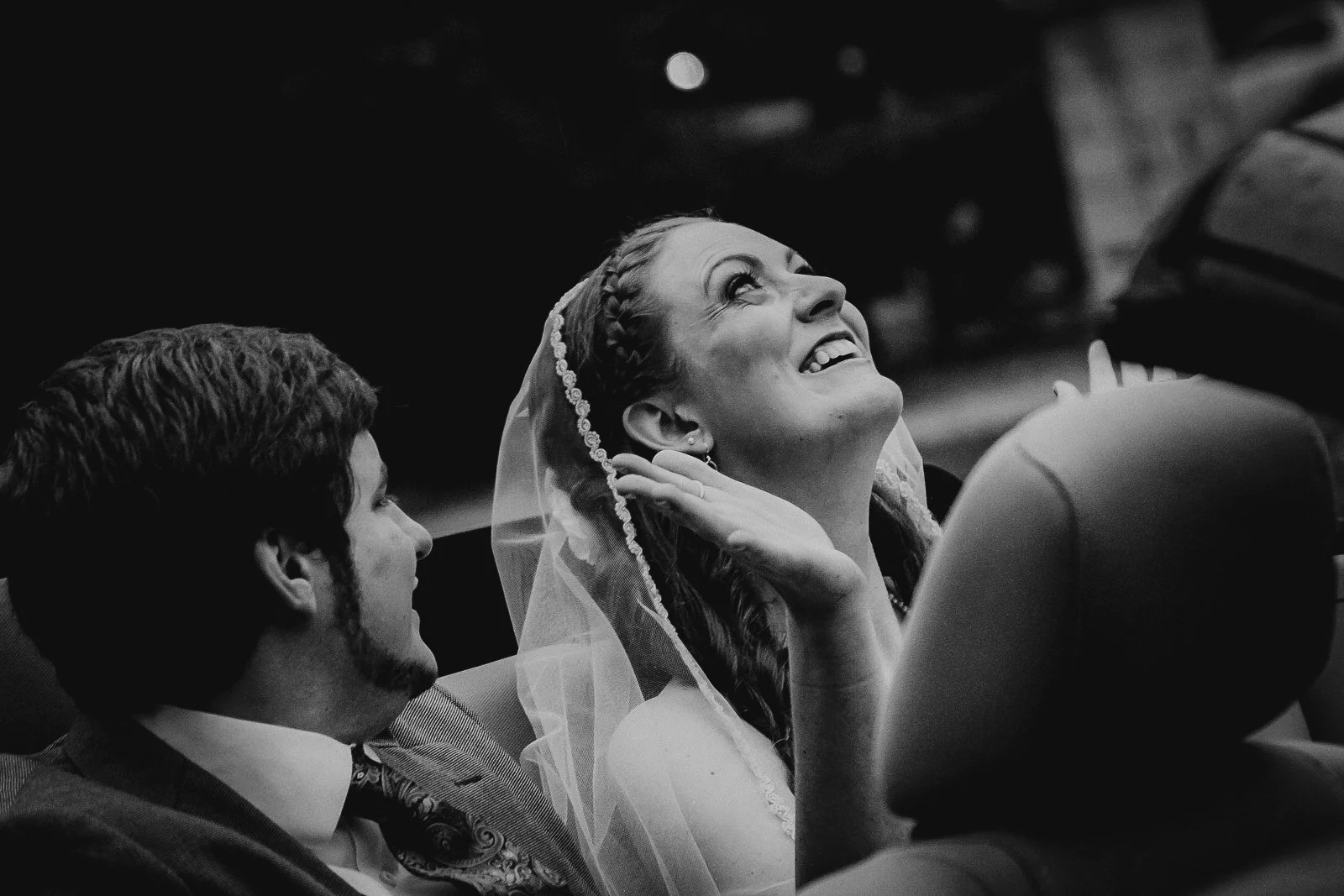 Black and white photo of a bride and groom, with the bride smiling and looking up, and the groom looking at her, during their wedding ceremony.