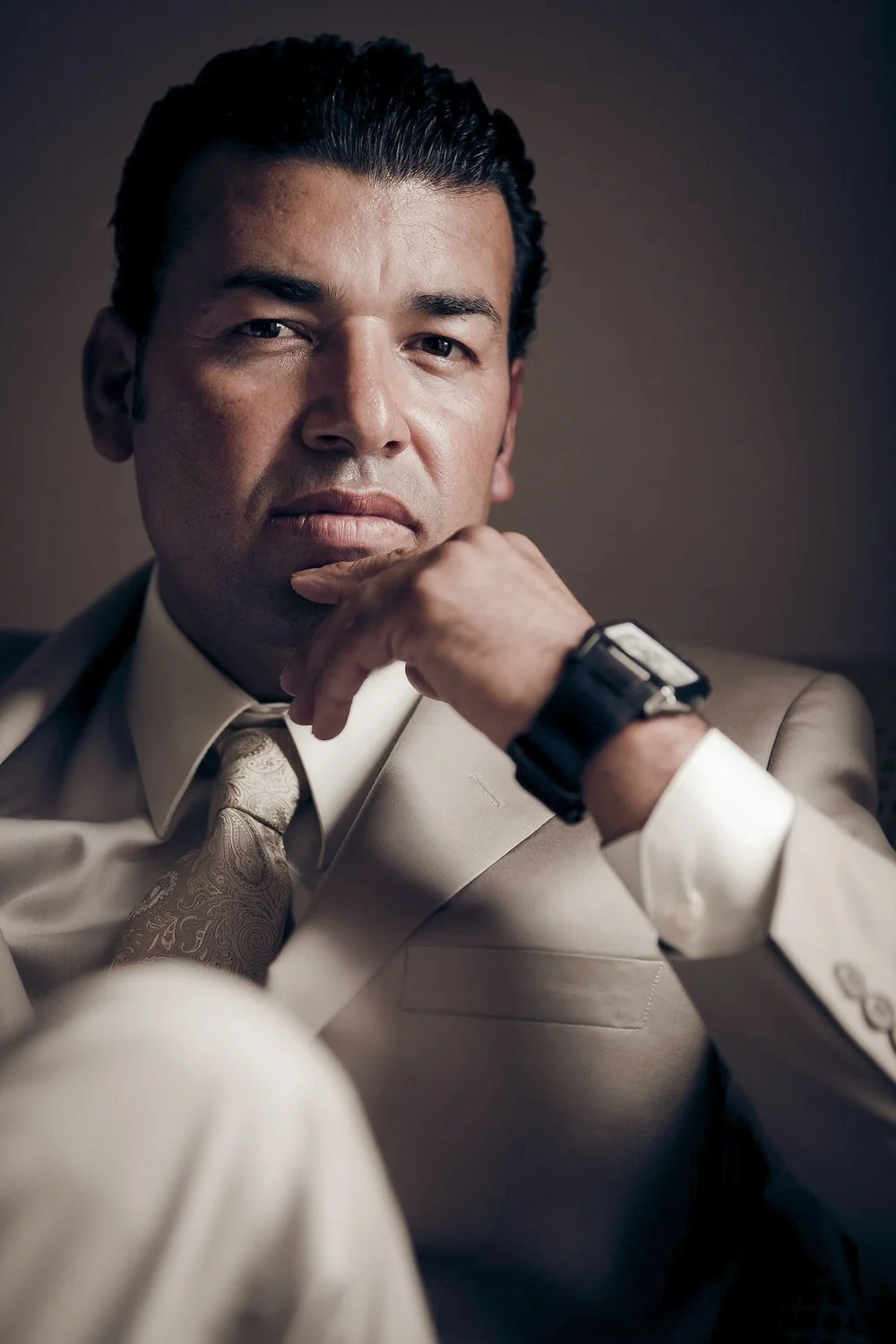 A portrait of a groom in a tan suit sitting in his hotel room.