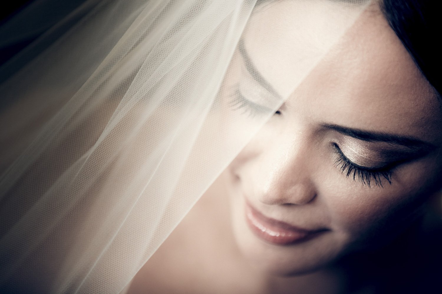 A close up of a bride's face adorned in full make up, with her dress' veil covering half her face.