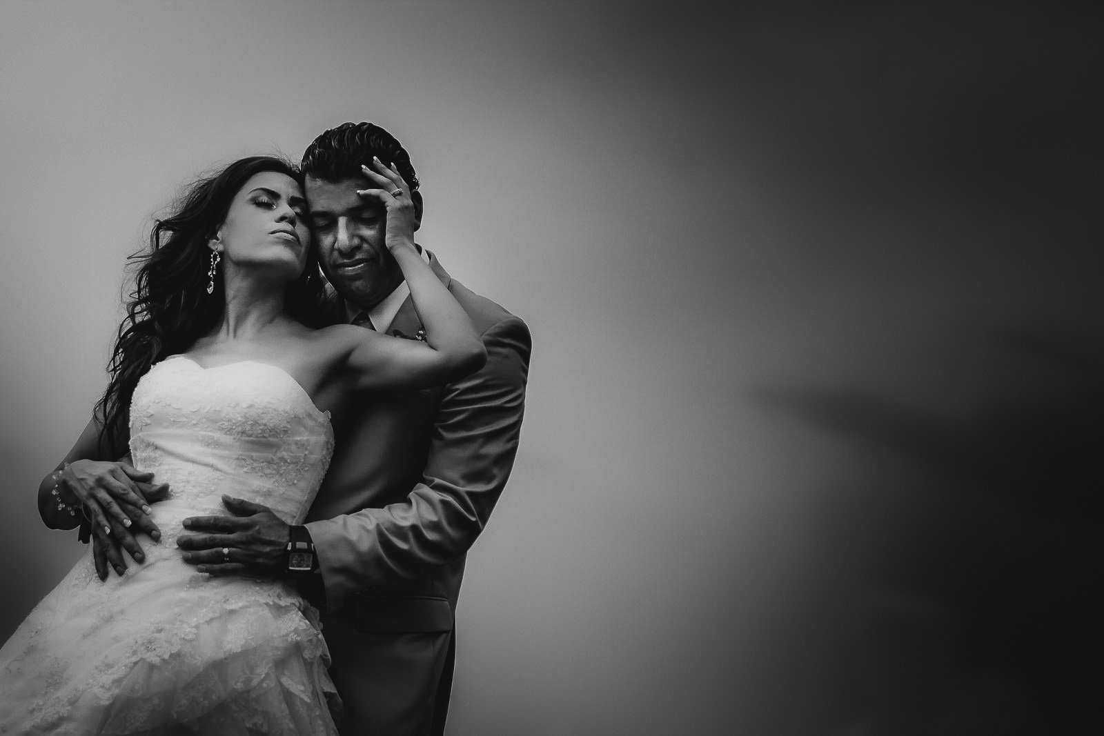 A black and white photo of a bride and groom in an emotional embrace, with the bride's hand on the groom's face and the groom's hands around her waist.