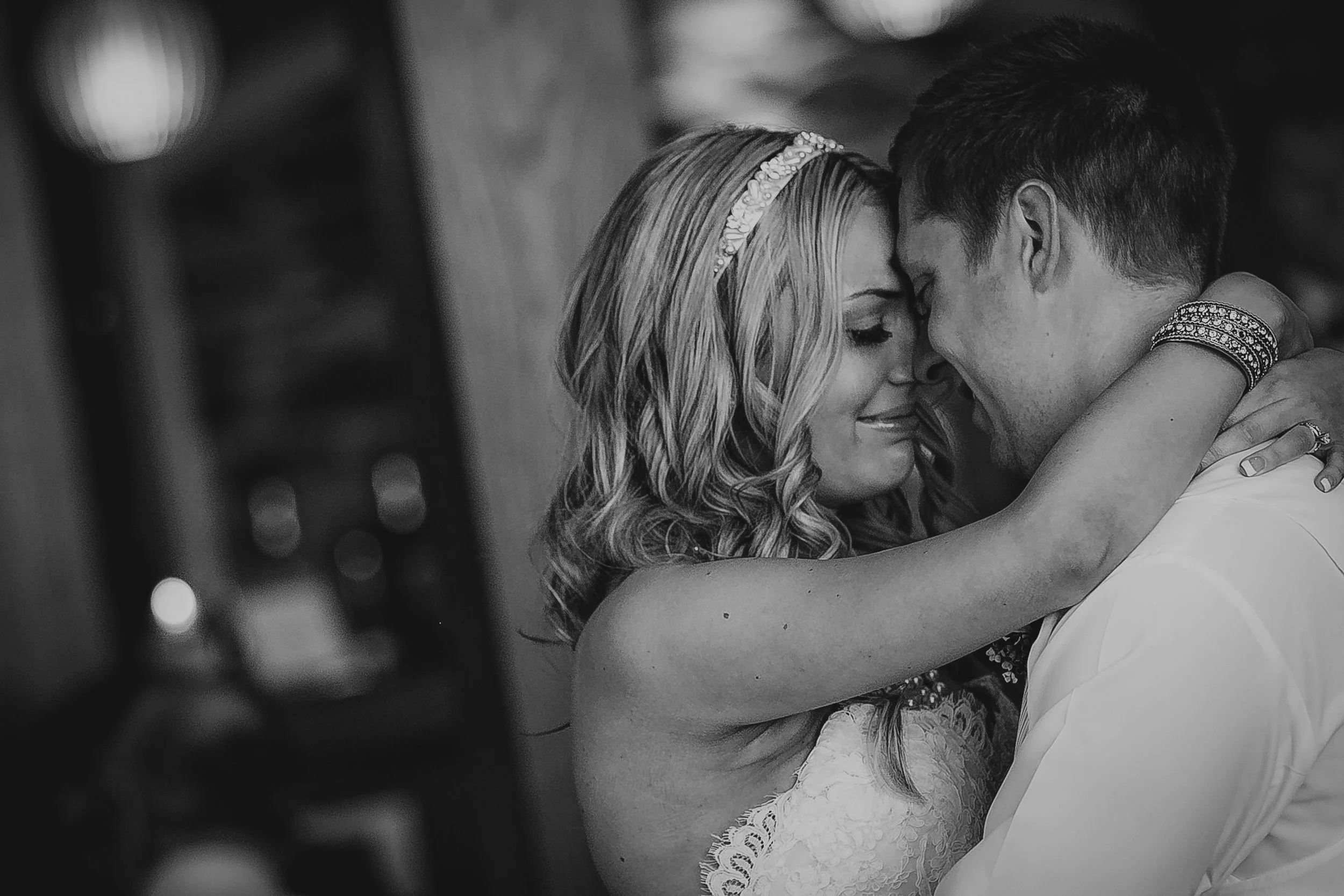 A black and white photo of a bride and groom embracing with foreheads touching, eyes closed, smiling softly.