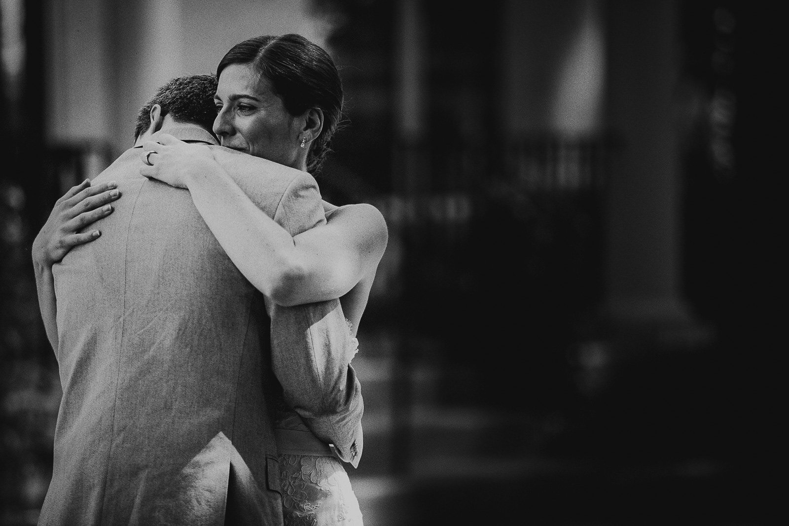 Black and white photo of a woman hugging a man. The woman has dark hair and is smiling with her eyes closed. The man is not visible.