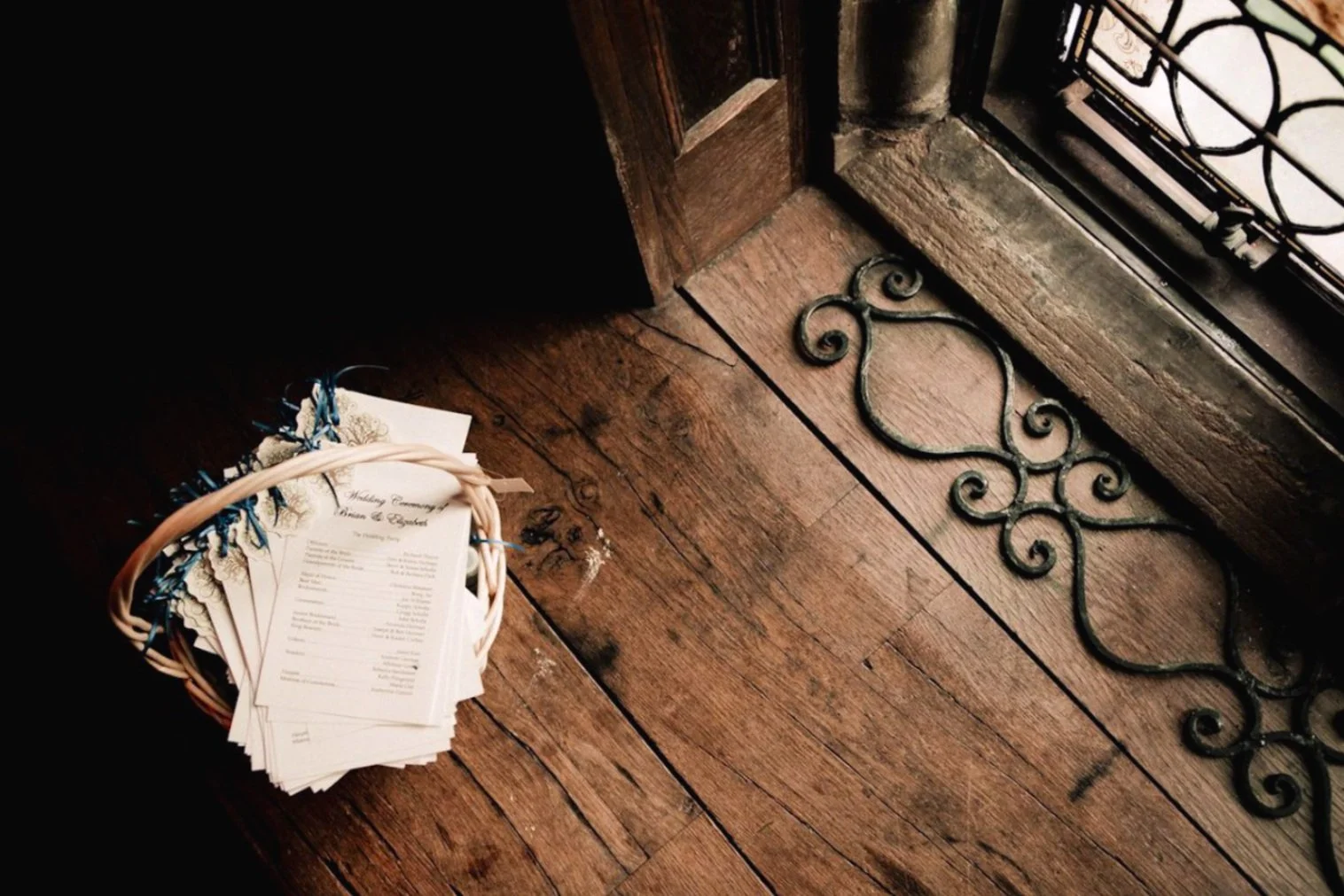 A basket of wedding ceremony programs sitting on a wooden floor by a window.