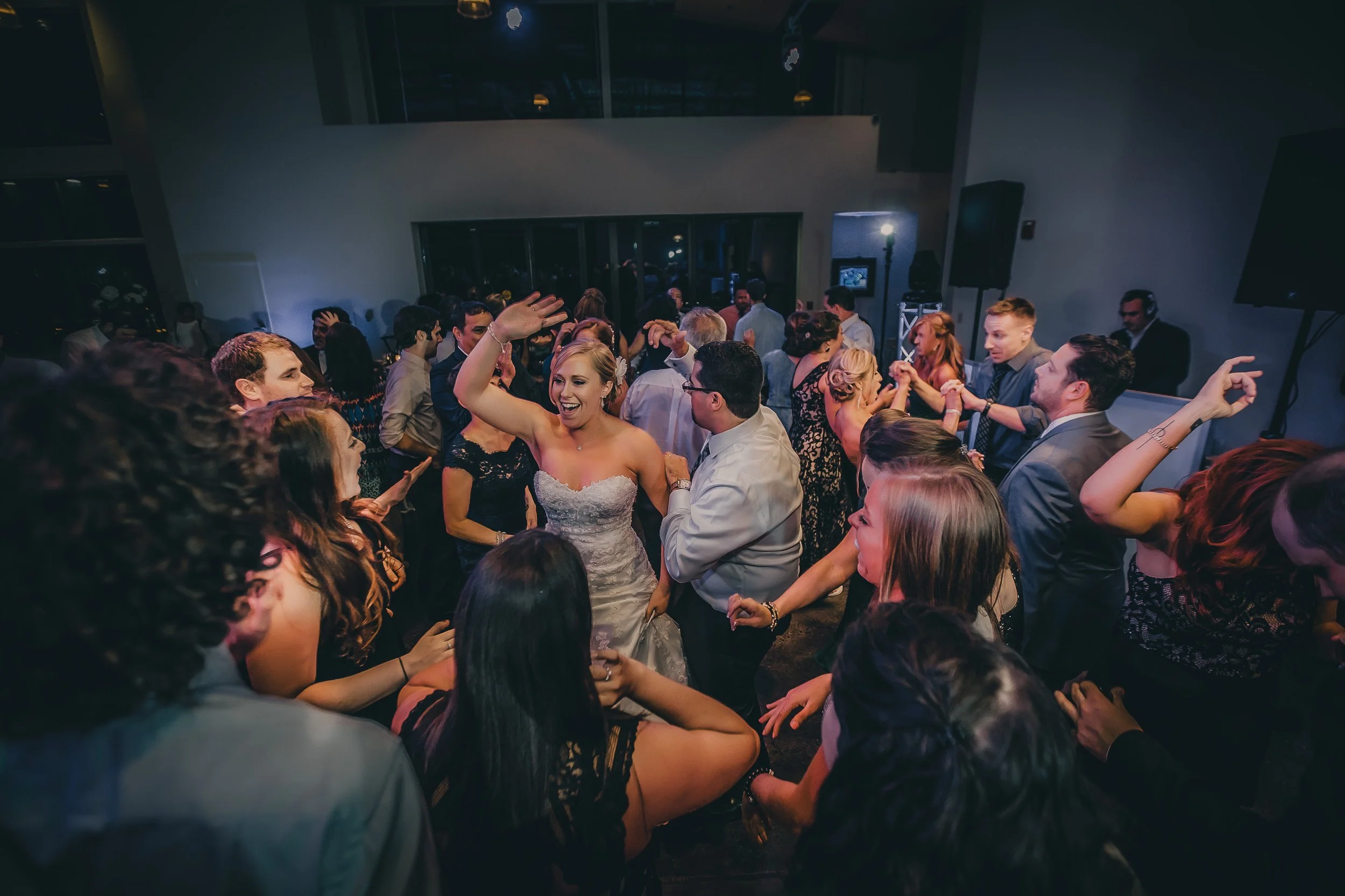 People dancing and celebrating at a wedding reception in a dimly lit indoor venue.