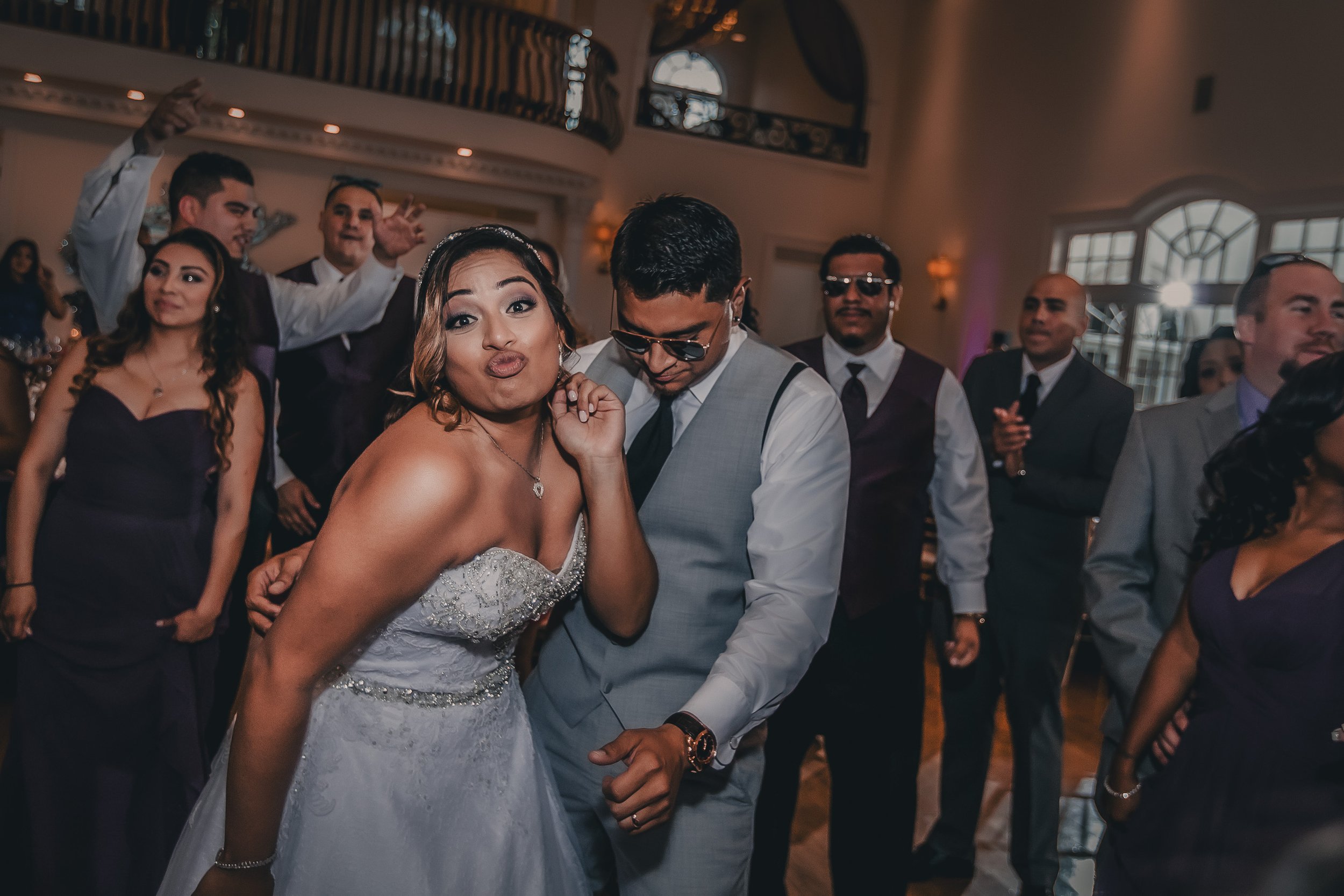 Bride and groom dancing at a wedding reception with friends and family in the background.