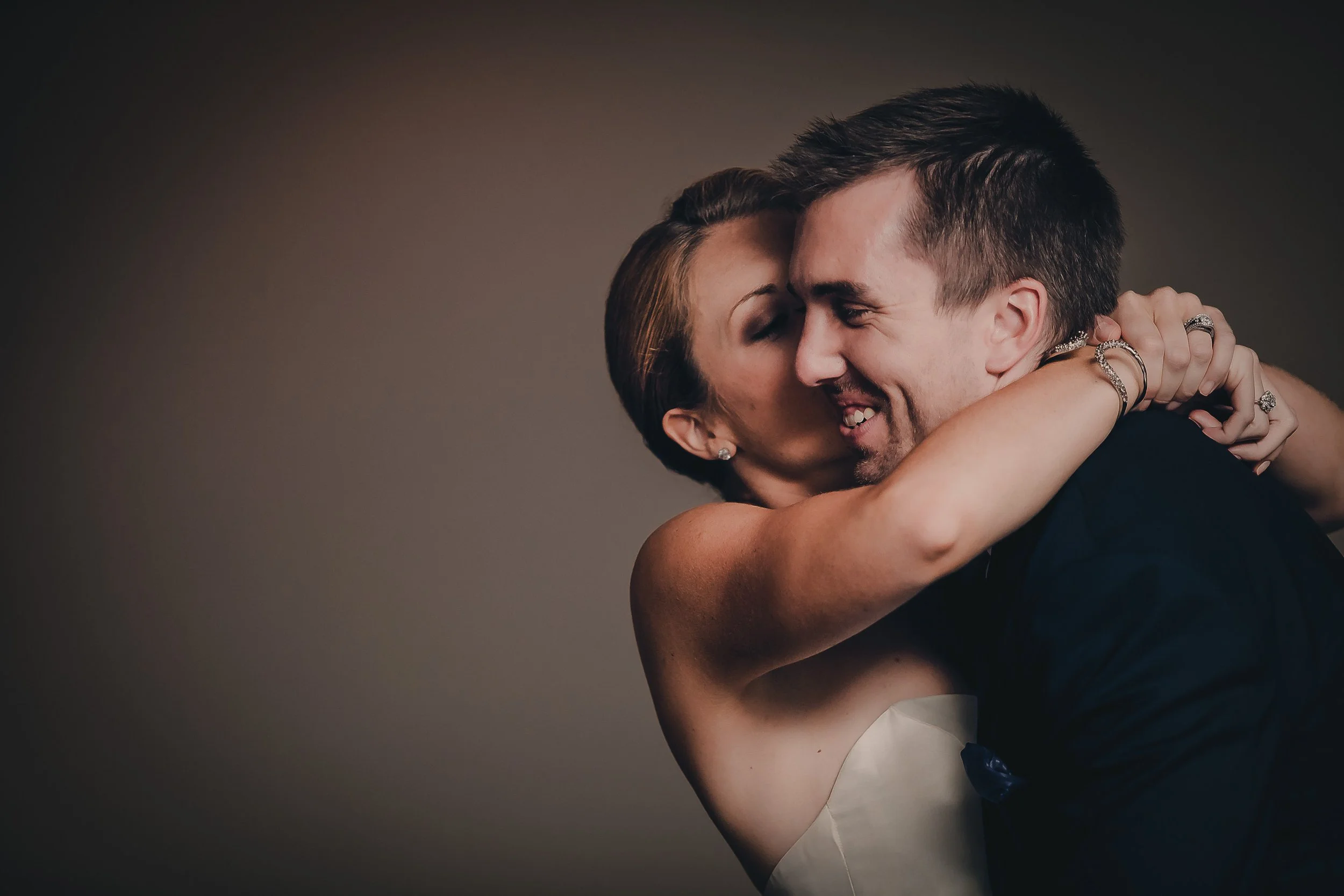 A couple sharing a close embrace, smiling with eyes closed, against a plain background.