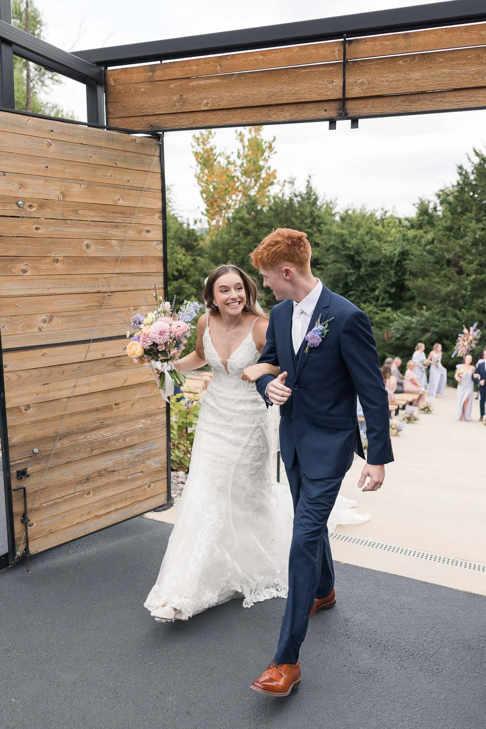 A bride and groom walking hand in hand at their outdoor wedding reception, smiling and looking at each other.