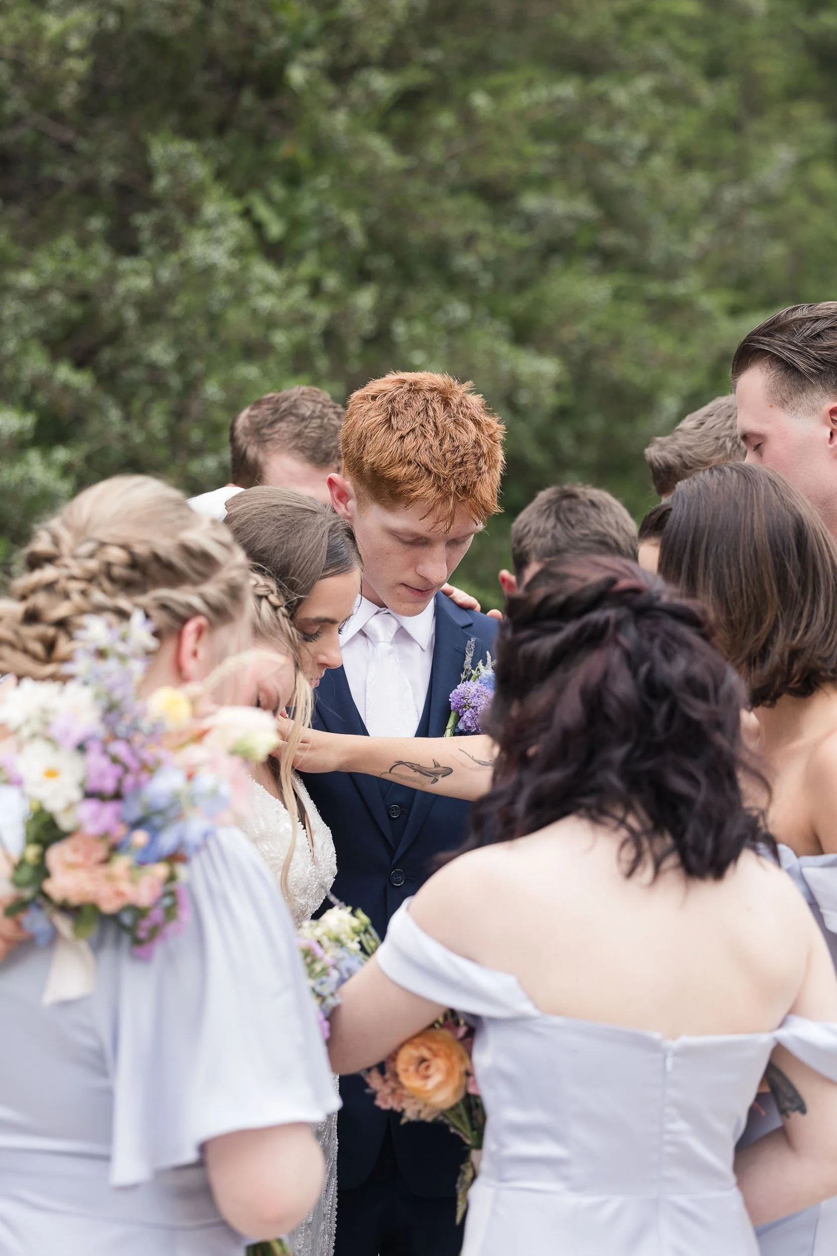 Couple in wedding attire sharing a kiss in the middle of a tree-lined paved path
