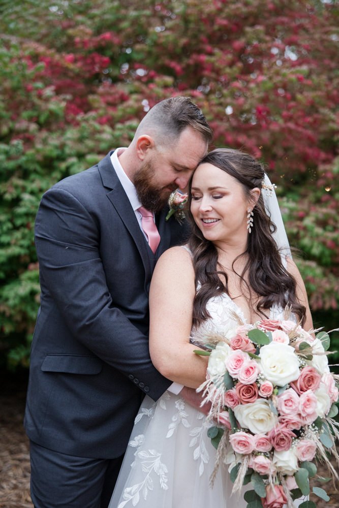 Bride and groom embracing with bouquet outdoors