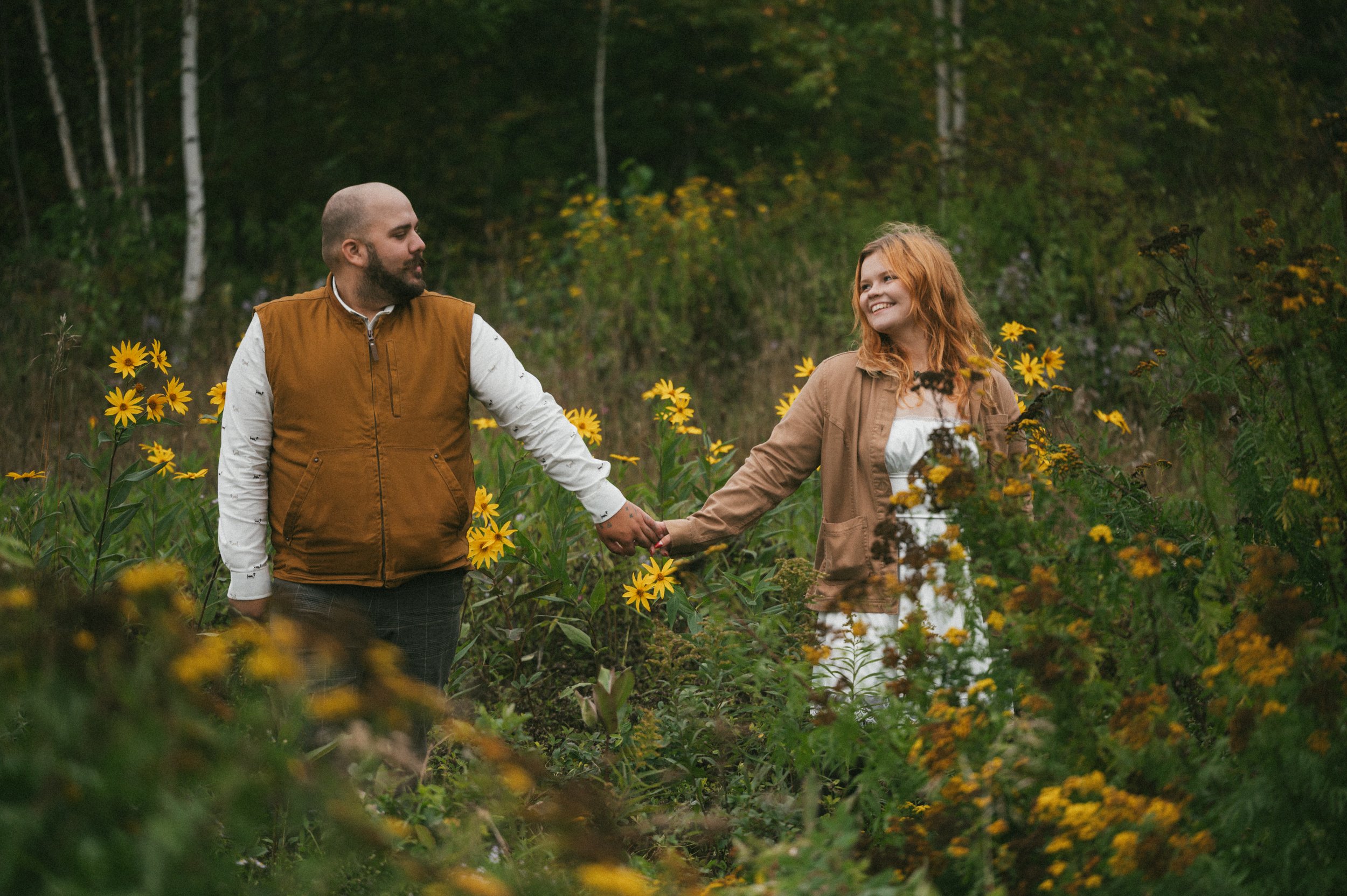 man and woman hold hand and smile at each other in a field of yellow flowers on mackinac island