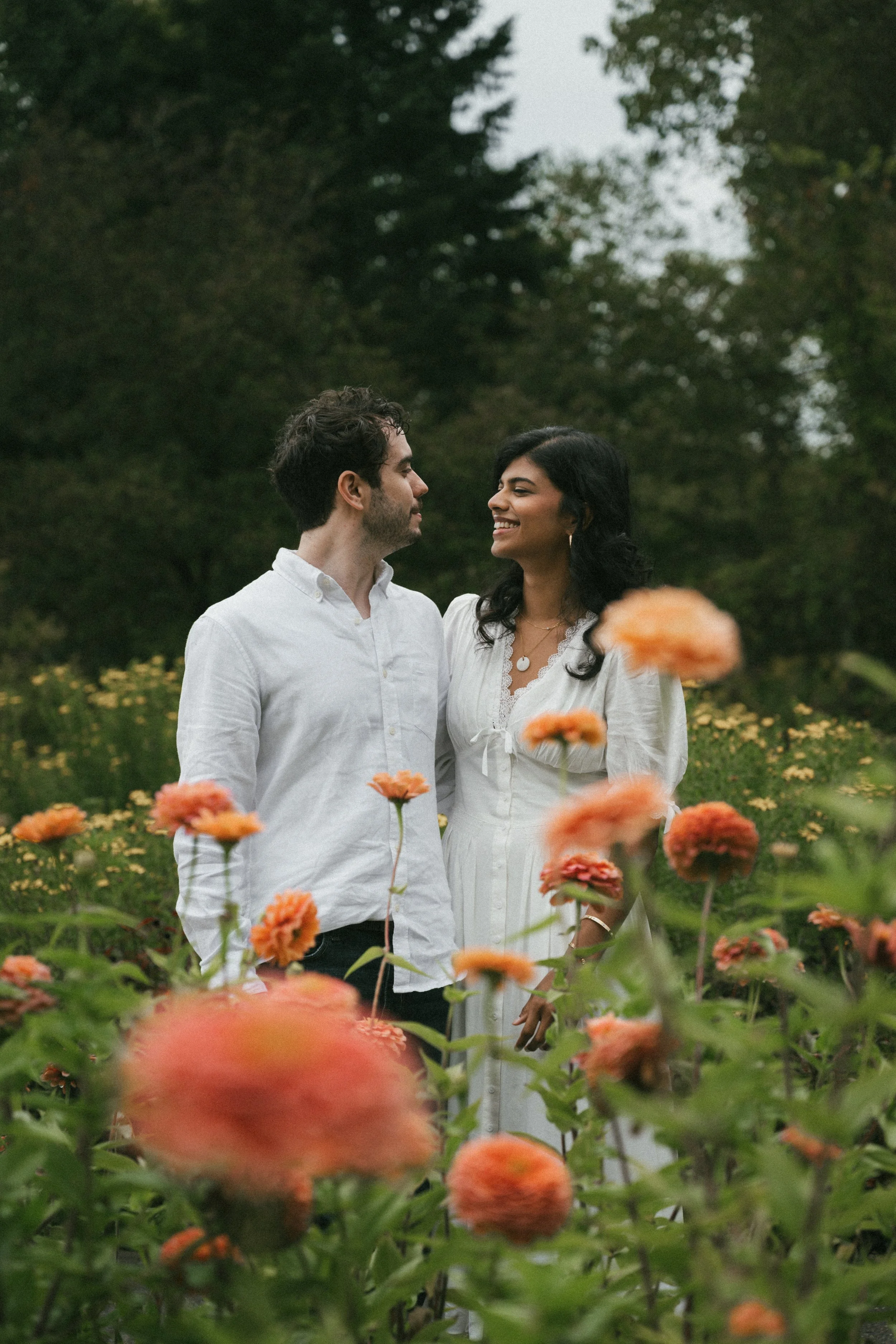 man and woman pose together in a flied full of orange zinnias