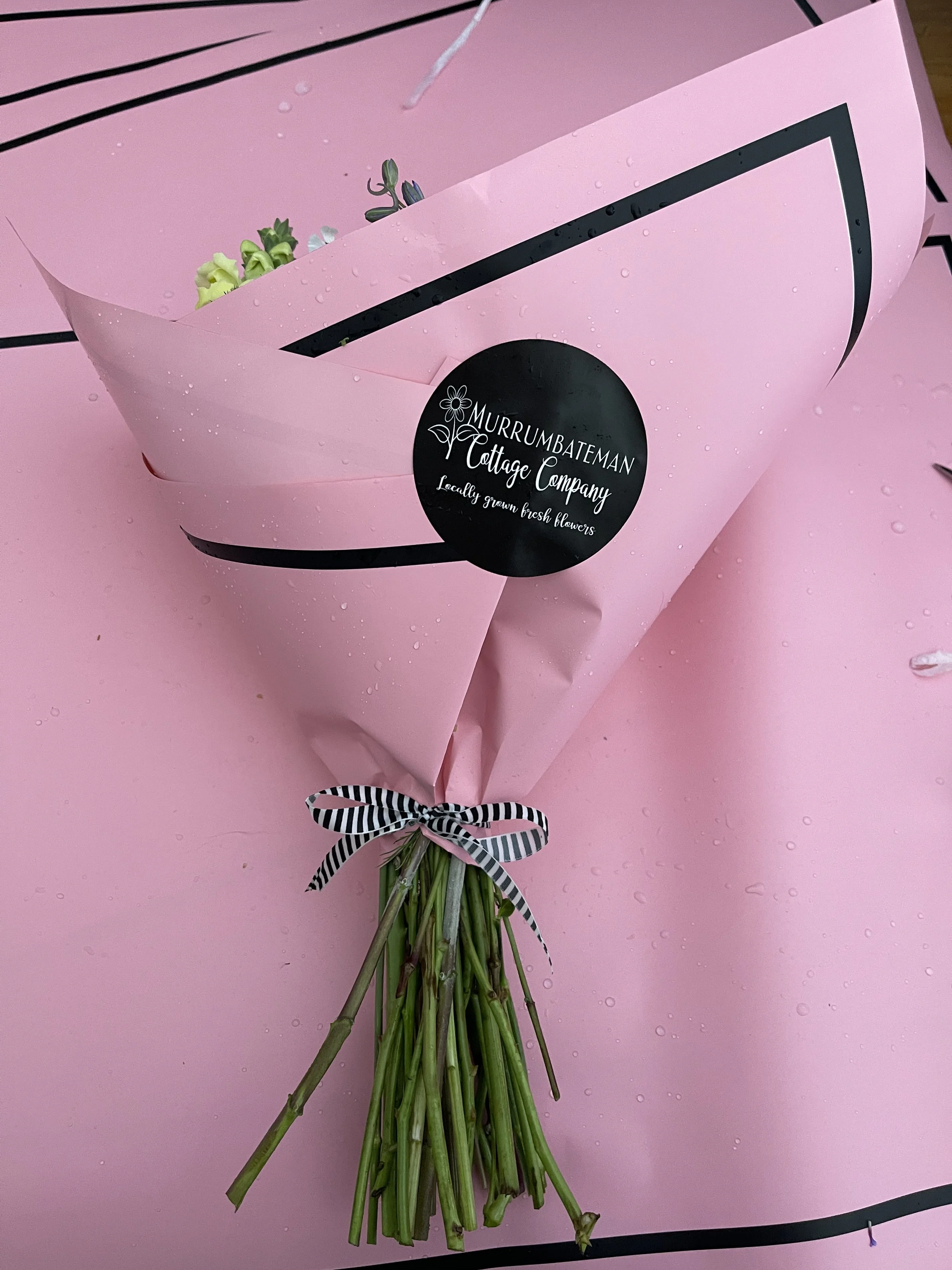 Bouquet wrapped in pink paper with "Murrumbateman Cottage Company" sticker and black-white striped ribbon.