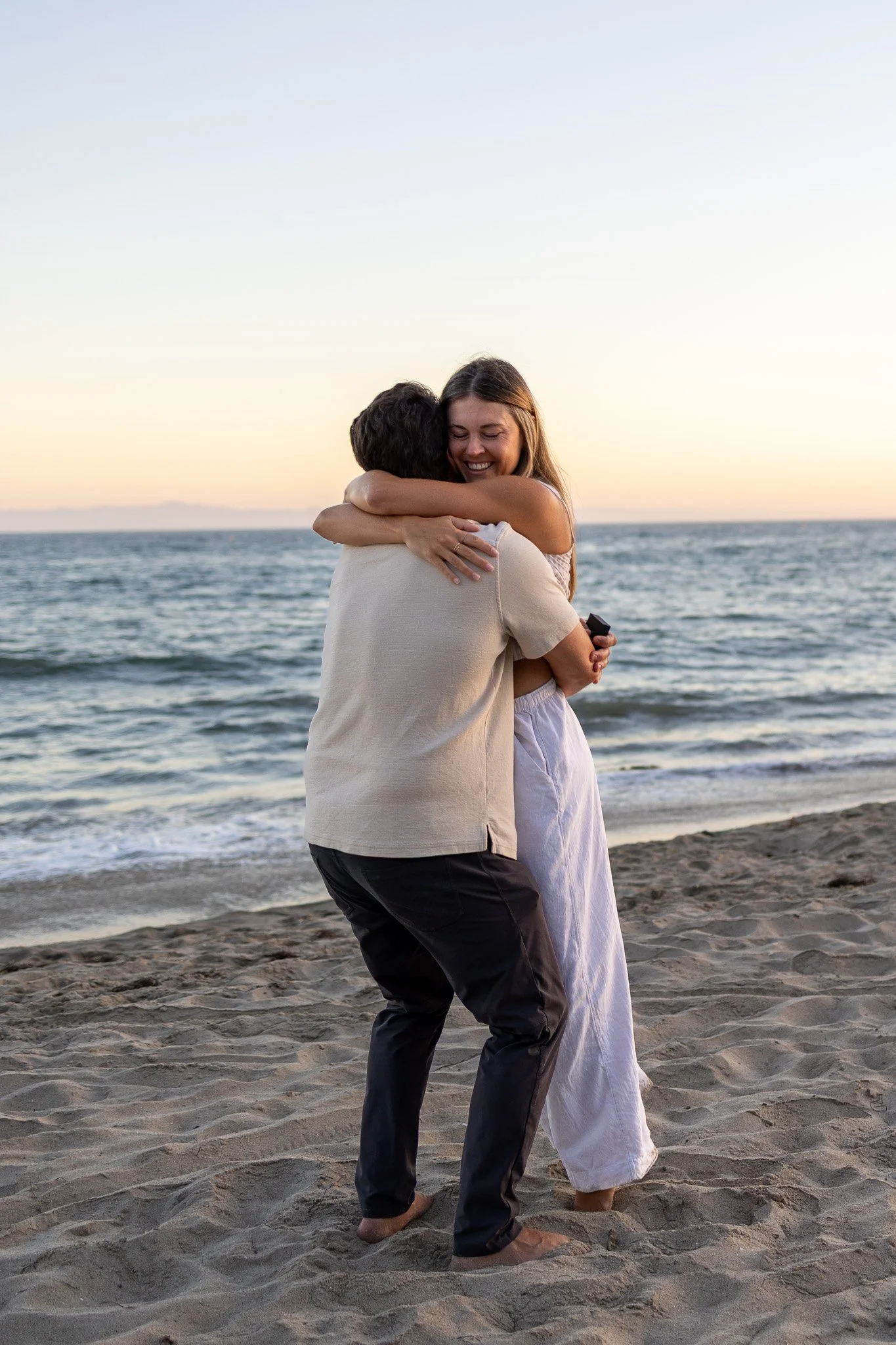 A couple embracing on the beach near the ocean during sunset.