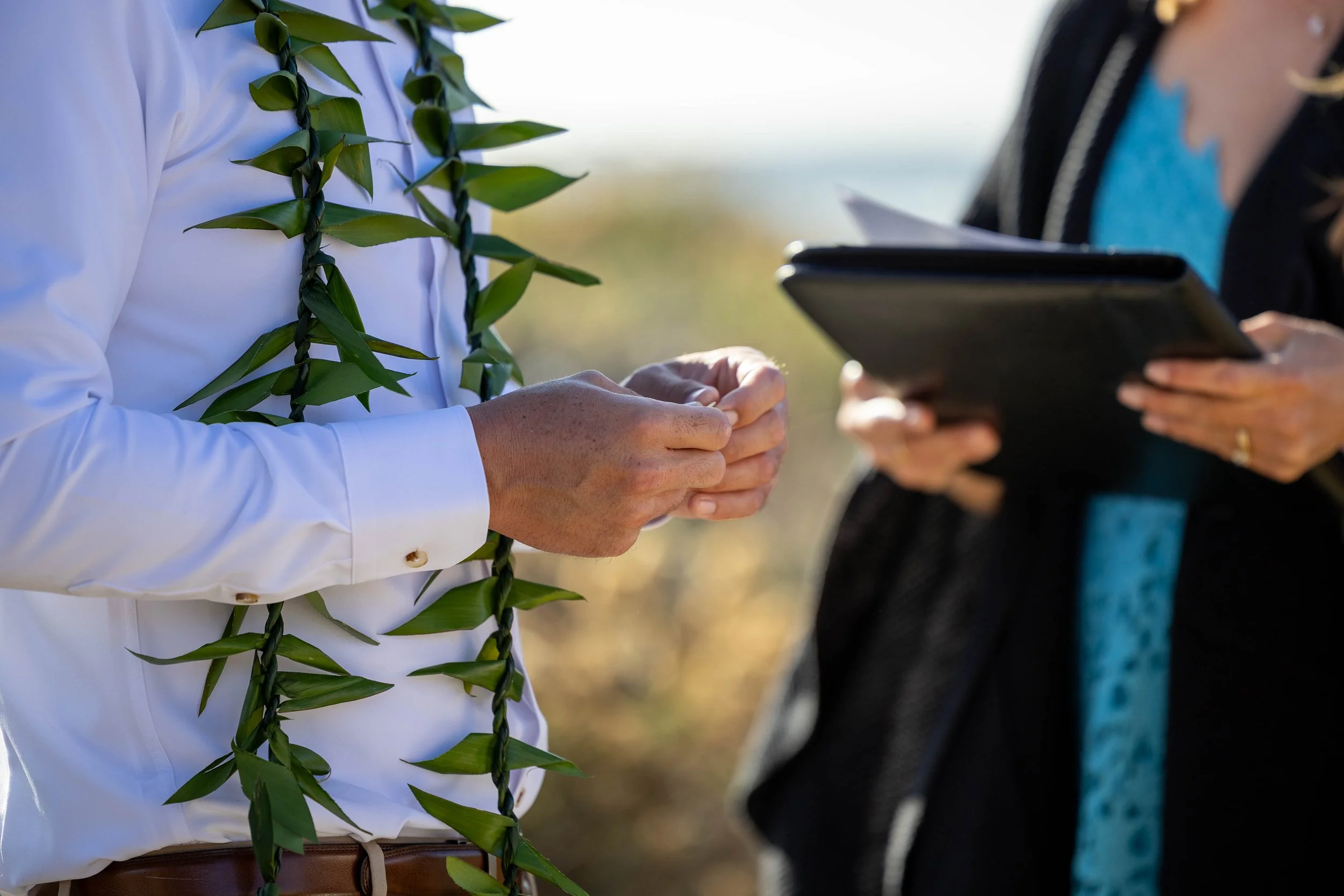 Person wearing a white shirt and a leafy lei administering an oath, with another person holding a tablet nearby.