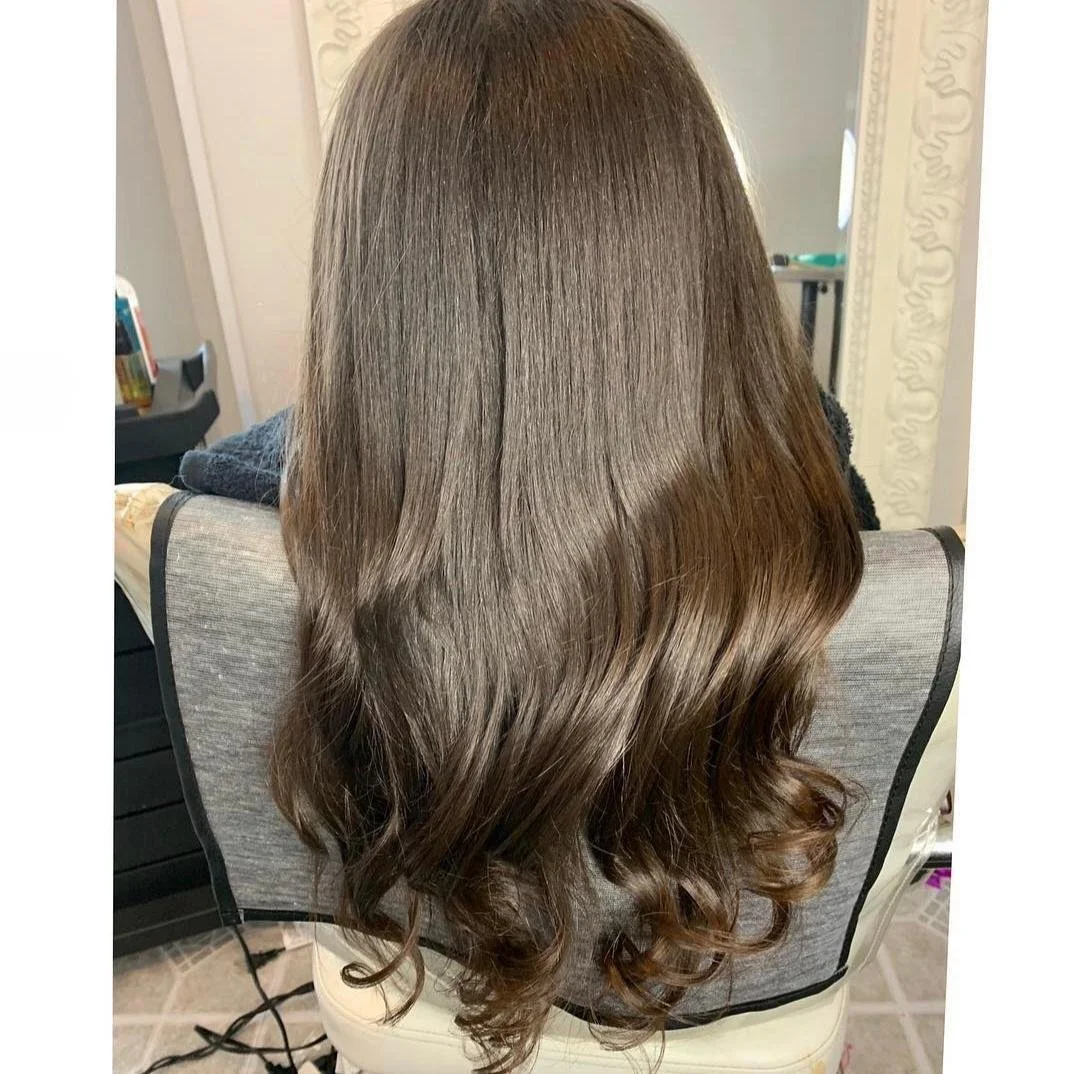 Back view of a woman with long, wavy, brown hair sitting in a salon chair.
