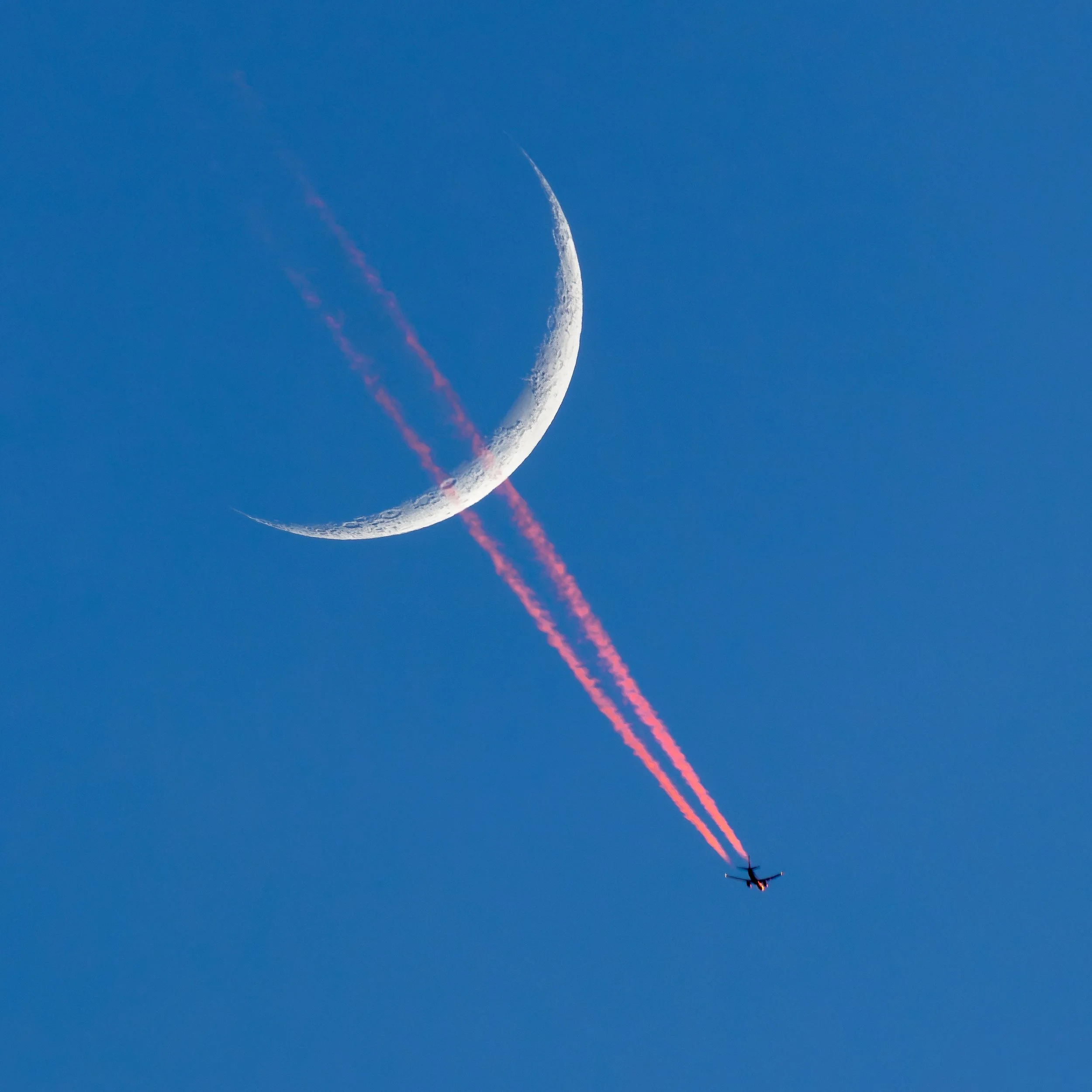 An aircraft leaves illuminated contrails as it transits past a waxing crescent moon over Washington, D.C., on December 22, 2025