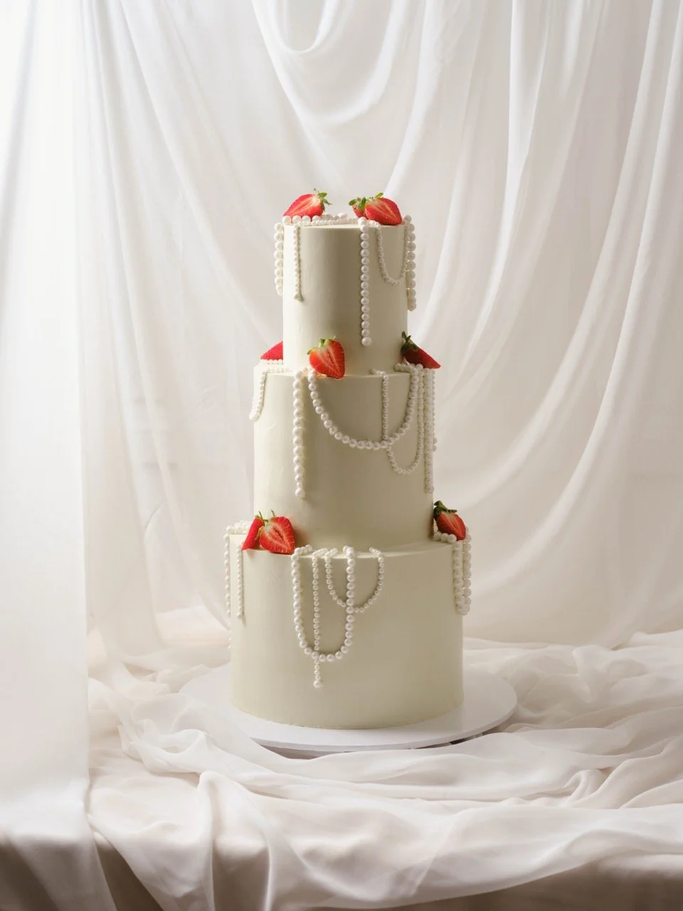 Three-tier white wedding cake decorated with strawberries and pearl strings.