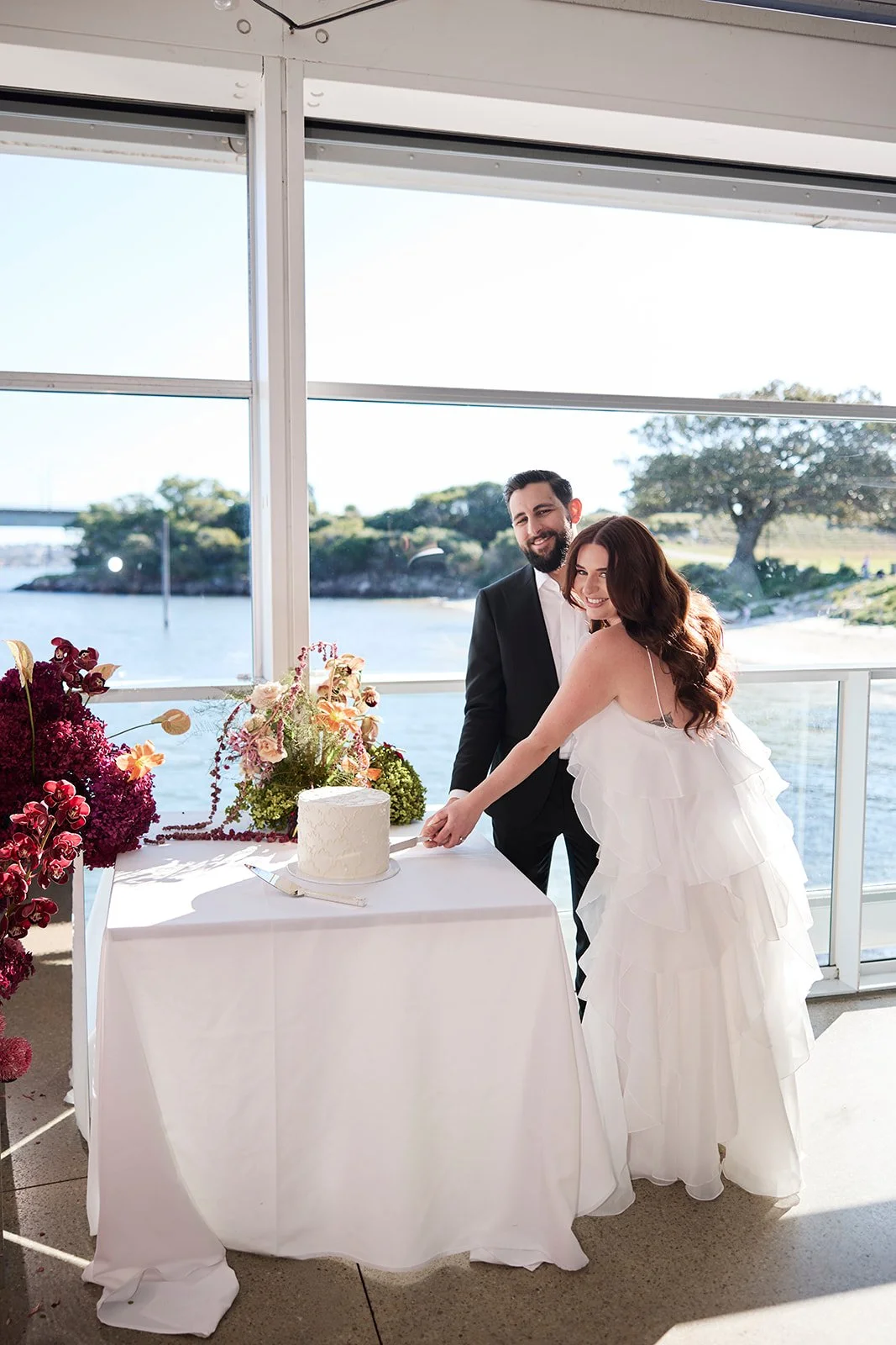 Couple cutting a single tier wedding cake in a white lace buttercream design at a waterside venue - photo by Mandy Wood