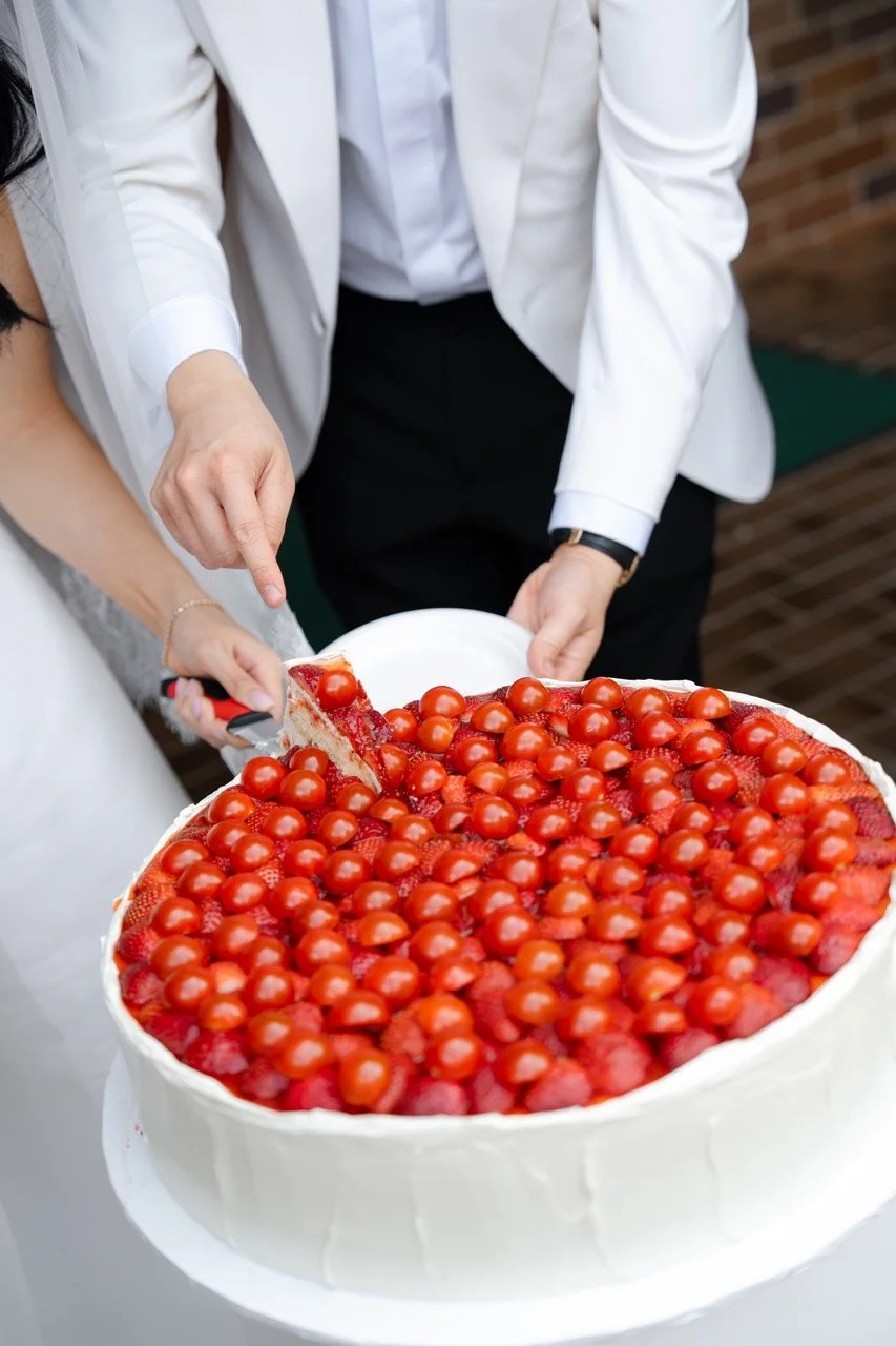 Couple cutting a wedding cake decorated with cherry tomatoes and strawberries