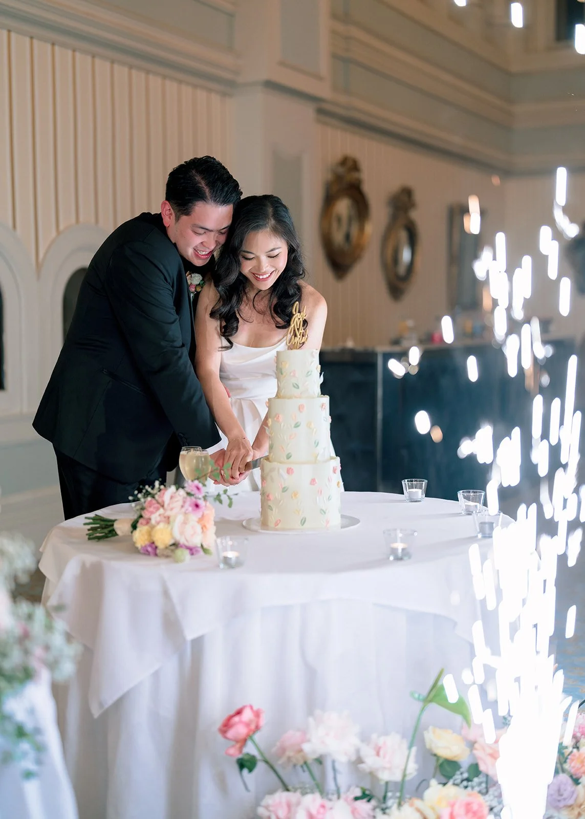 Couple cutting a three tier wedding cake with a pastel floral buttercream design - photo by Pepper June