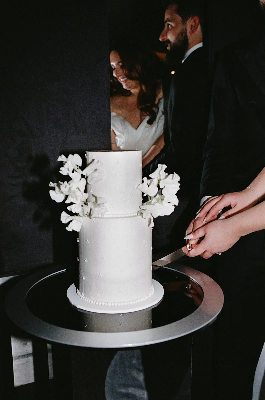 Couple cutting two tier wedding cake with flowers and delicate dotted pearl design - photo by Mandy Wood