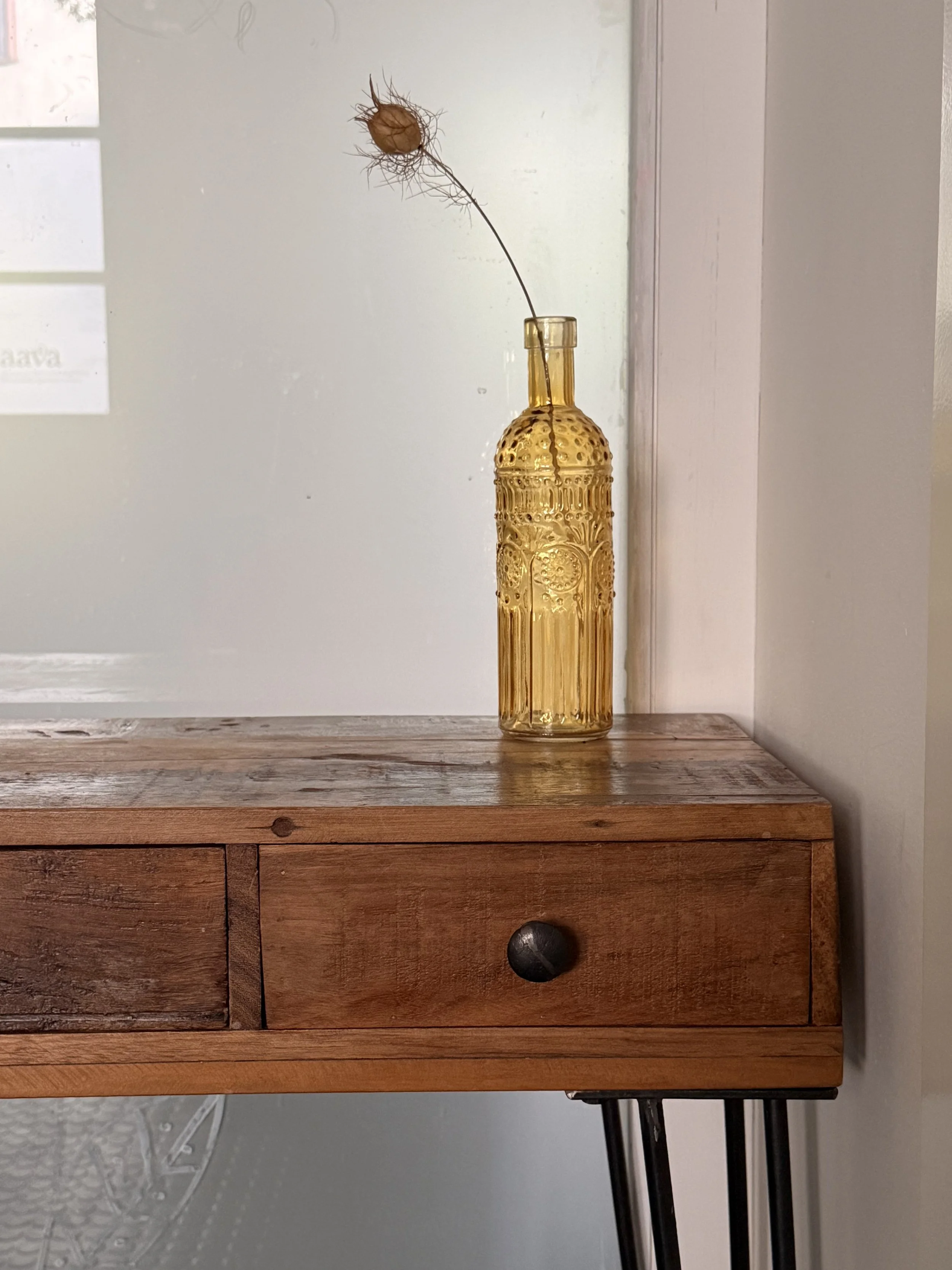 Ein braunes altes Glasflasche mit einer zarten Blume darin, auf einem Holztisch gegen eine Wandgestellt.