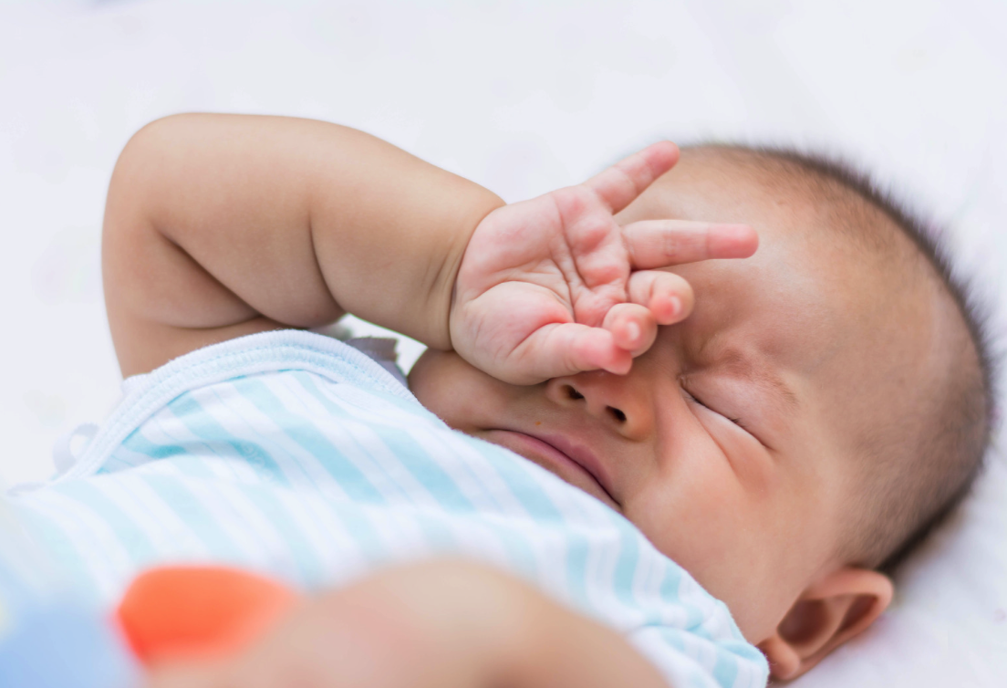 Nahaufnahme eines schlafenden Babys mit Hand vor dem Gesicht, im Hintergrund weißer Hintergrund.