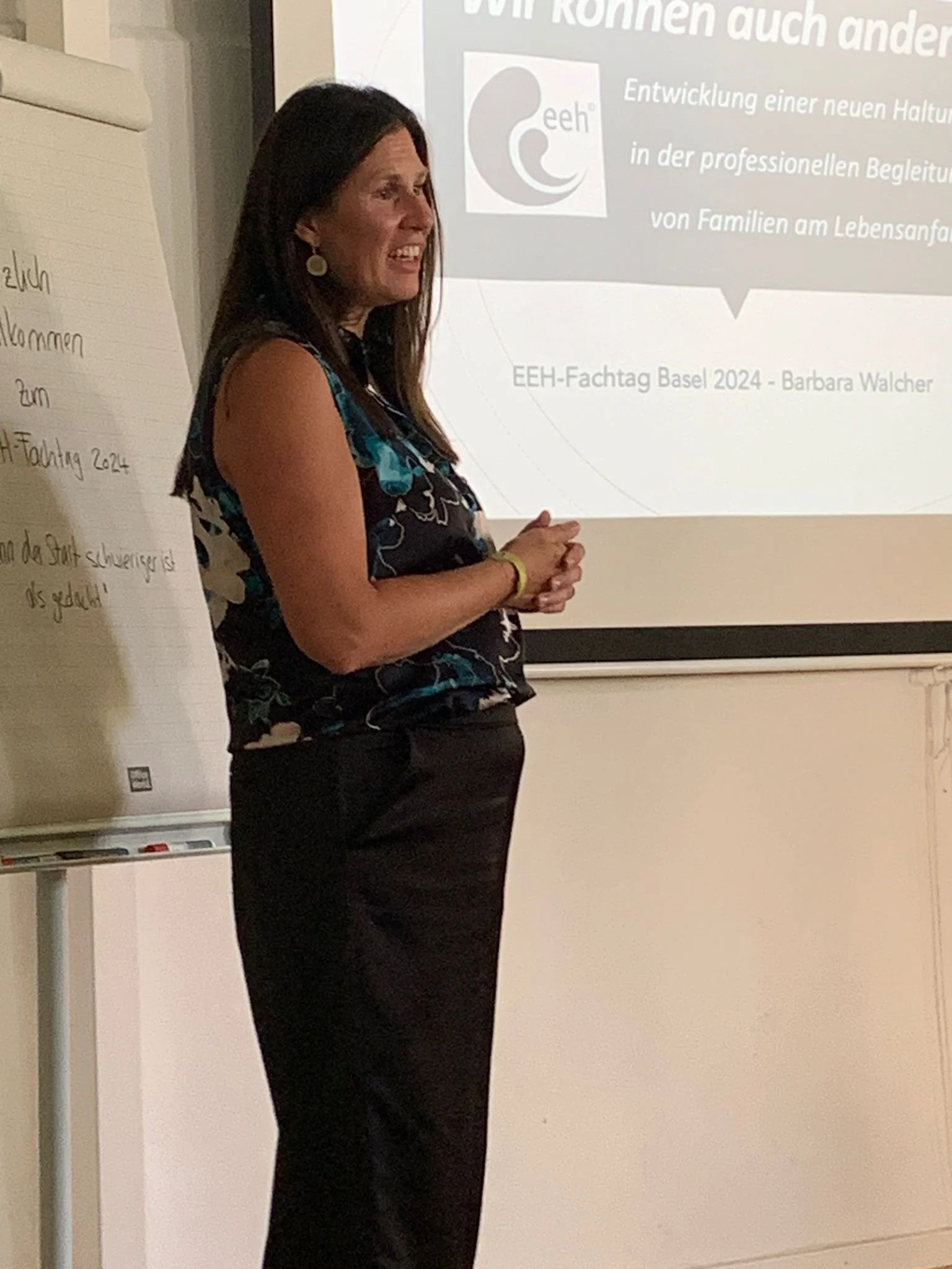Eine Frau steht vor einer Präsentation und spricht während eines Seminars im Raum.