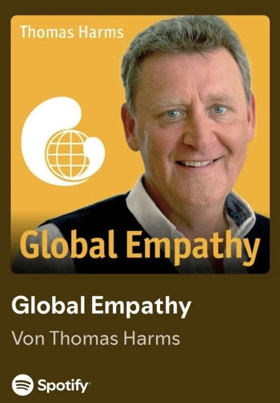 Das Bild zeigt das Cover eines Buches namens »Global Empathy« von Thomas Harms. Es enthält ein Foto eines Mannes, der in die Kamera lächelt, vor einem orangefarbenen Hintergrund mit einem weißen Logo, das eine Weltkugel umkreist, und dem Titel in großen gelben Buchstaben.