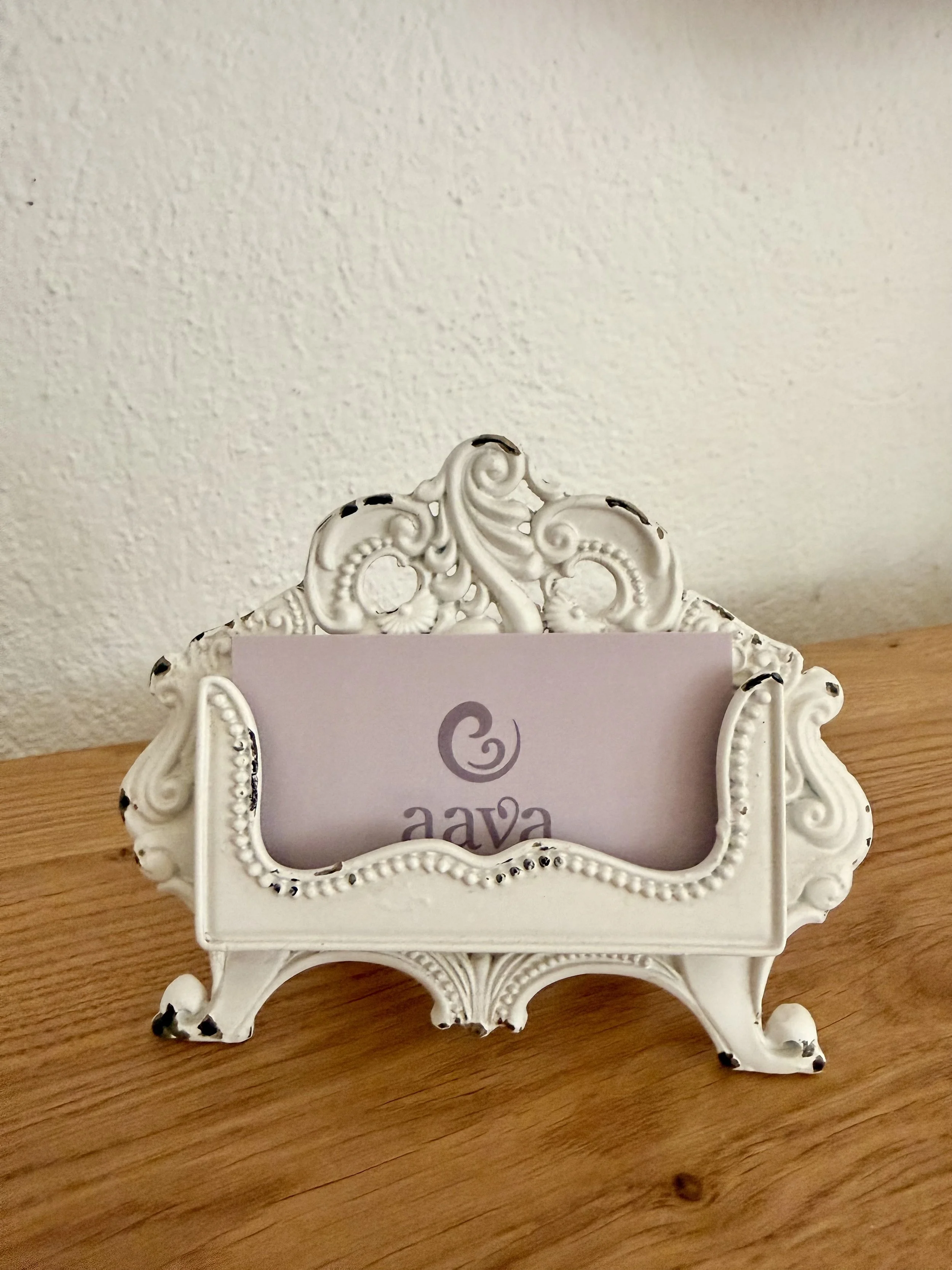 Hübscher, weißer, verzierter Schmuckständer mit einem Namensschild, auf Holzoberfläche mit weißer Wand im Hintergrund.