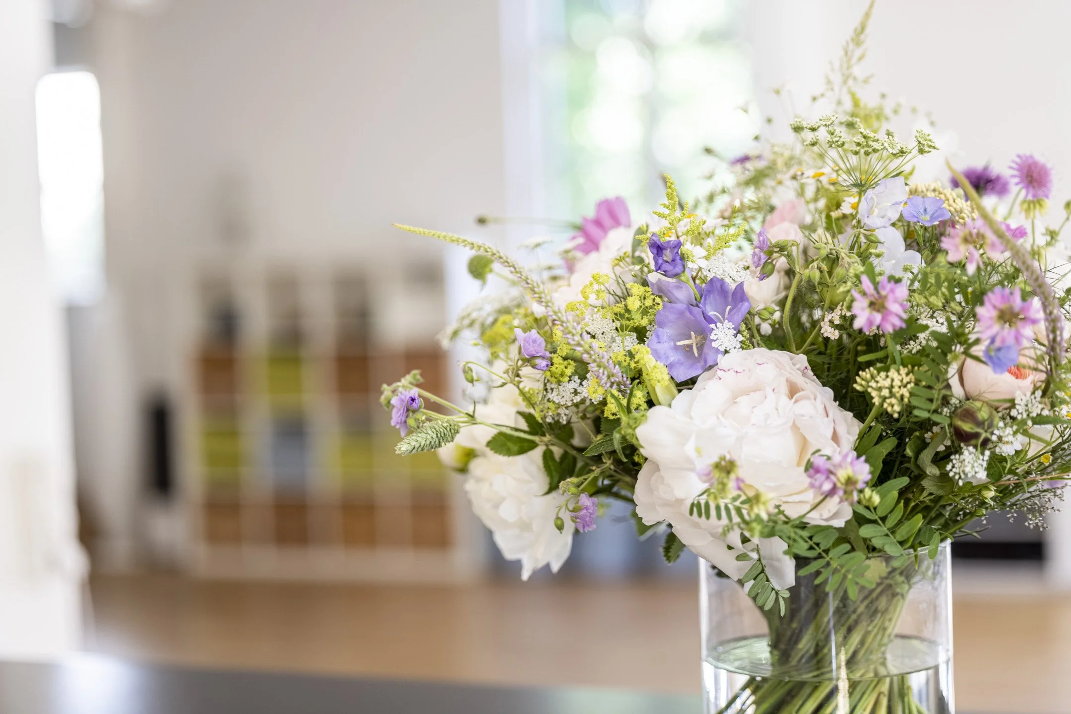Ein Strauß bunter Blumen in einer klaren Vase auf einem Tisch.