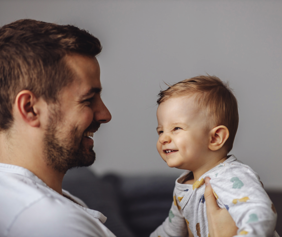 Ein Mann hält ein lachendes Baby in den Armen, beide schauen sich an.