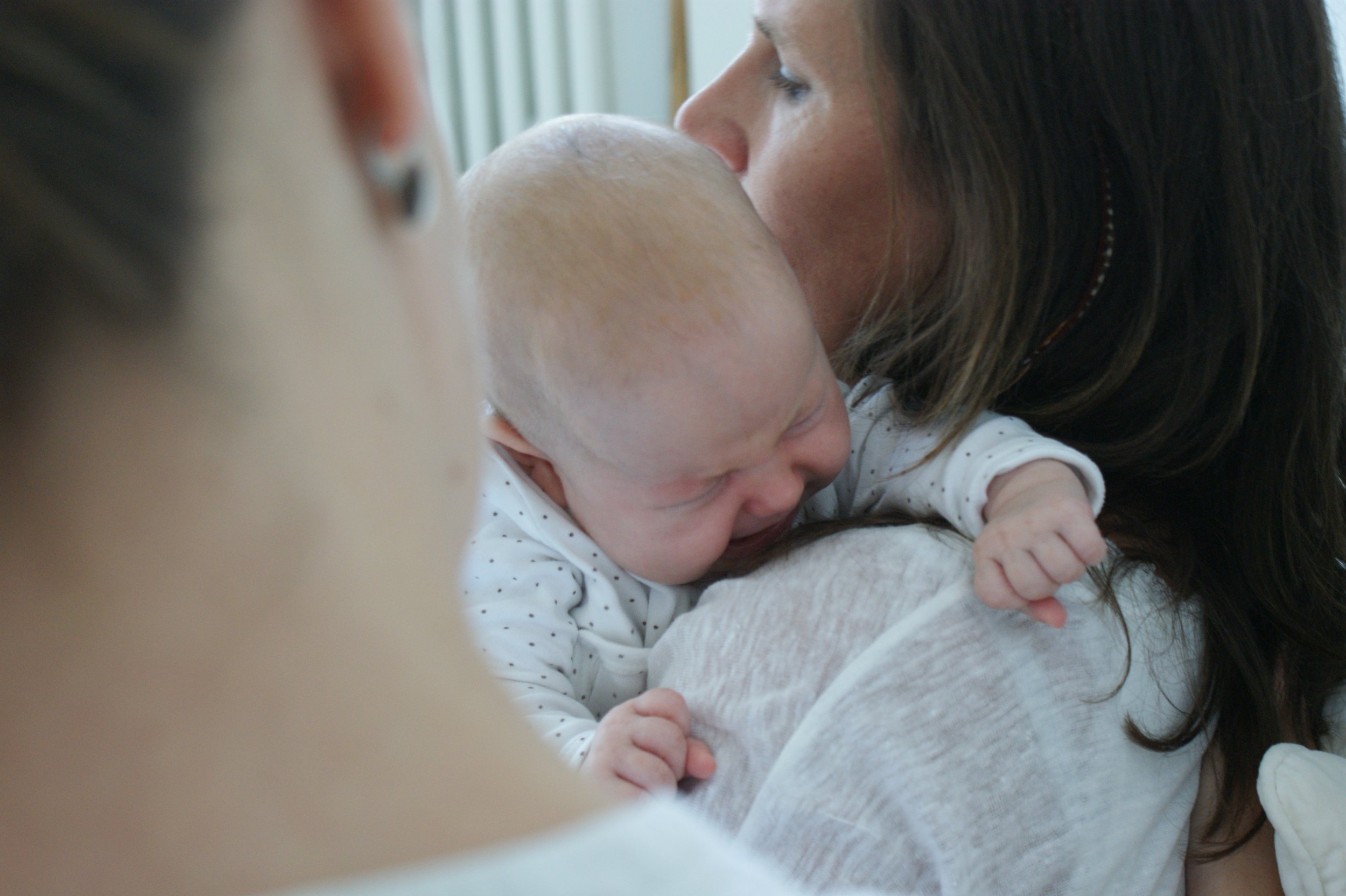 Eine Frau küsst ein Baby auf den Kopf, das an ihrer Schulter liegt. Der Moment wirkt liebevoll und intim.