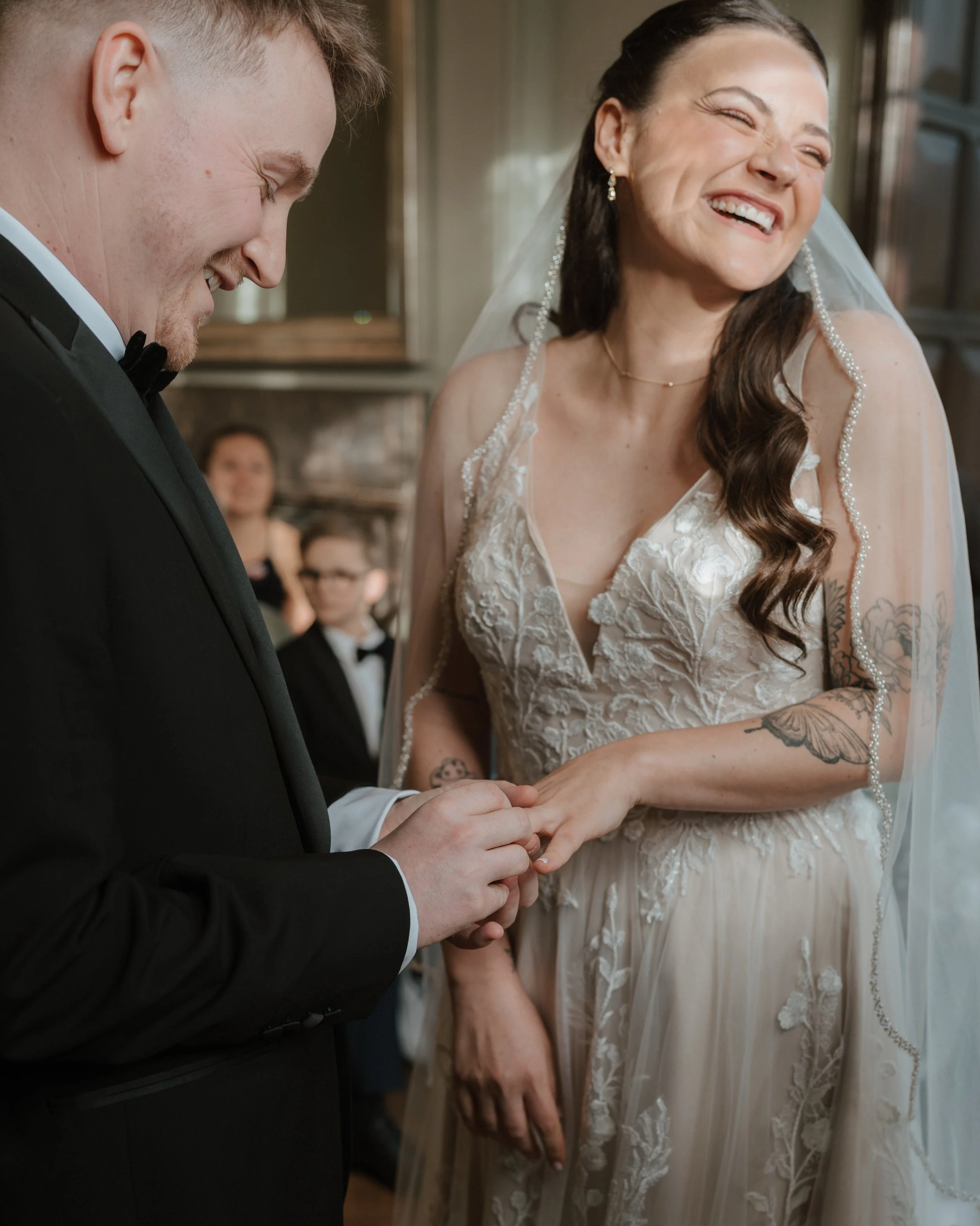 A groom is placing a wedding ring on a bride's finger during a wedding ceremony, both smiling joyfully at lewes registry office