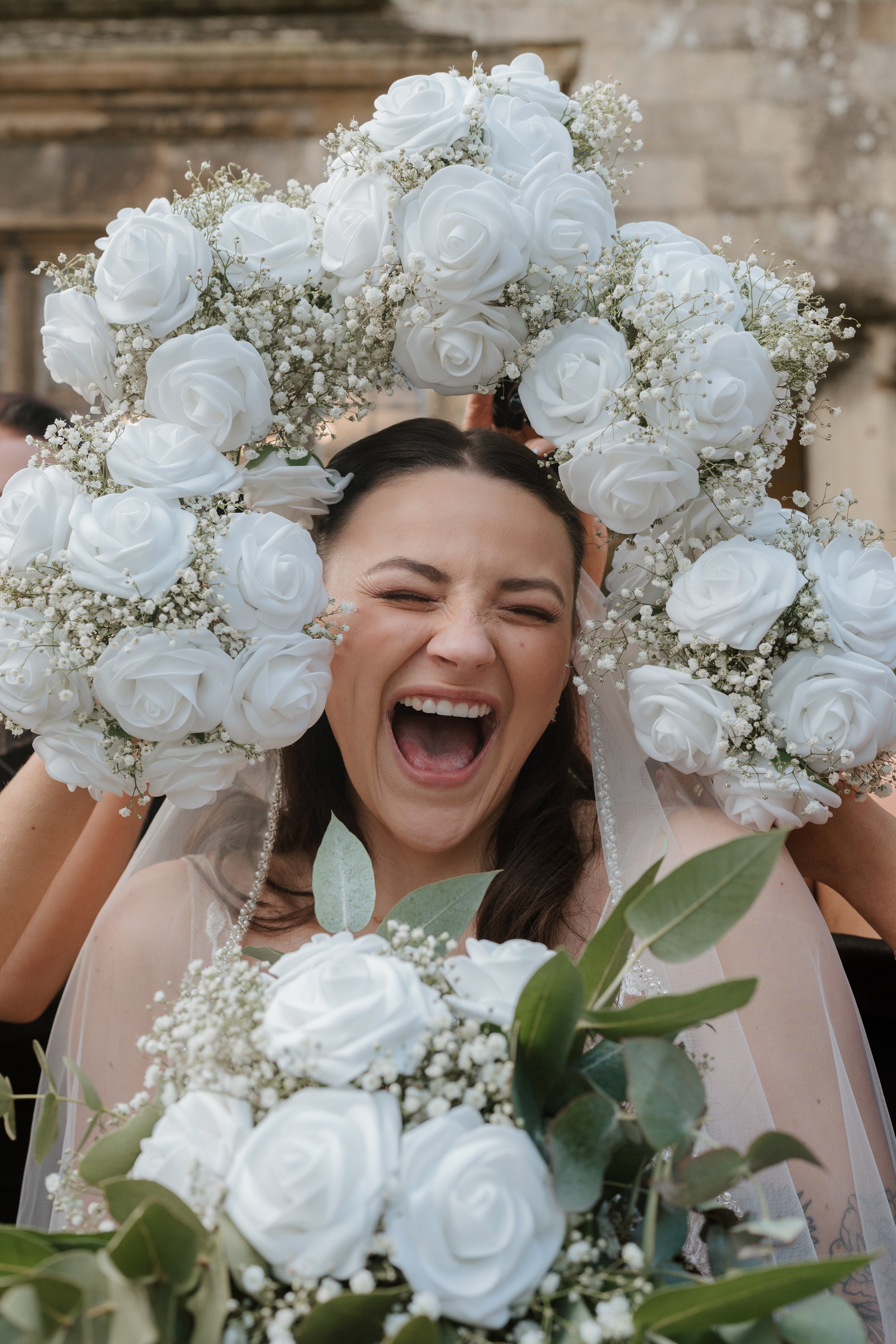 A bride celebrating her wedding, smiling widely, surrounded by a floral arrangement of white roses and greenery at eastbourne