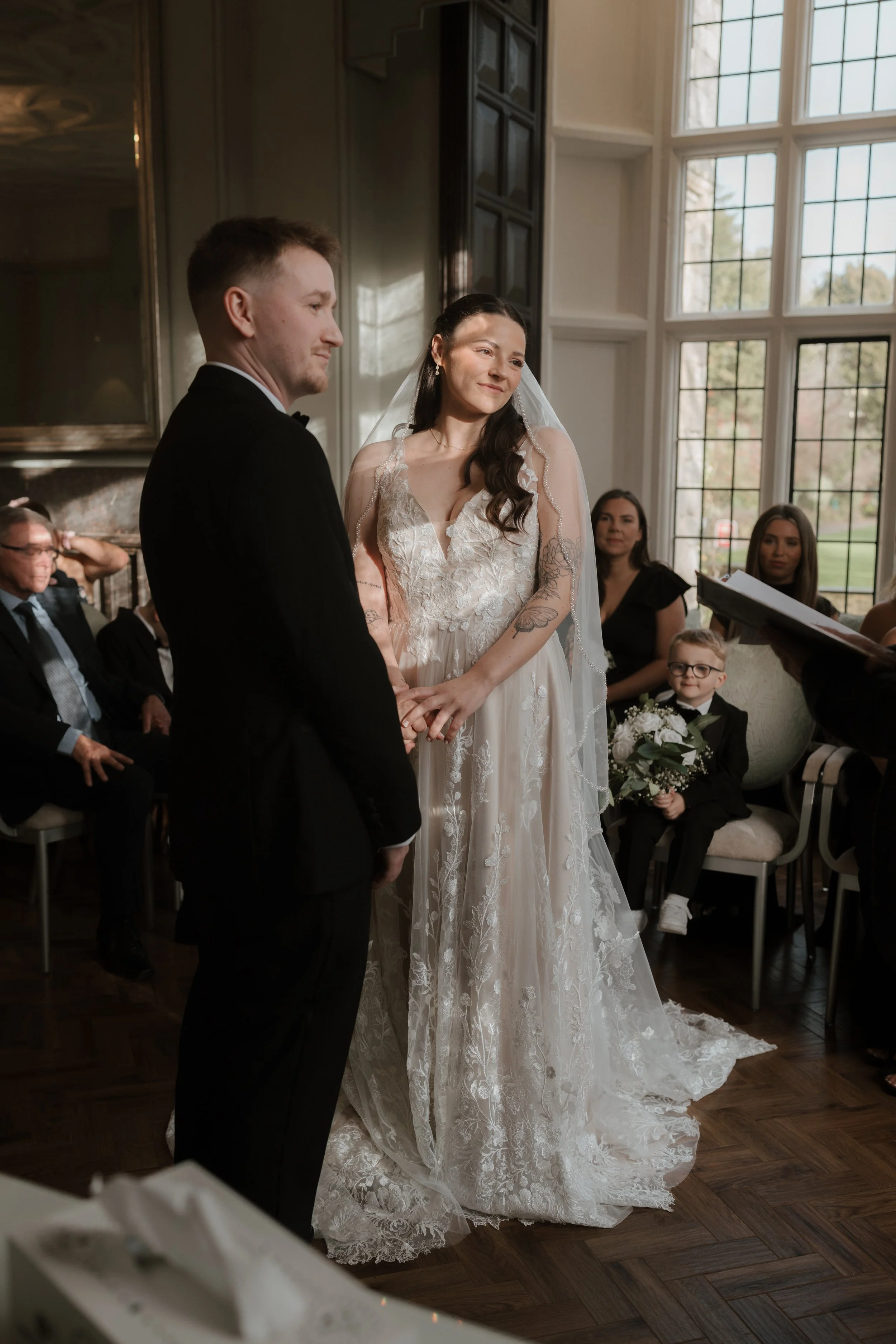A bride and groom exchange vows during their wedding ceremony in a bright, elegant room with large windows in bury st edmunds registry office