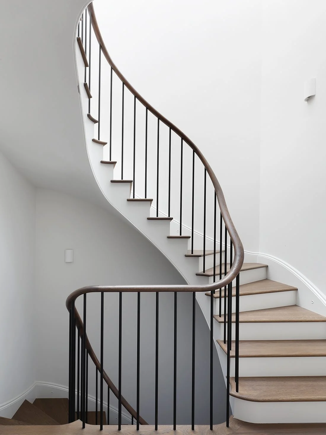 Taking inspiration from a nautilus shell, this staircase winds upwards and downwards in a beautiful curve. The continuous smoked oak handrail matches the timber treads and flooring to create harmony. Designed in collaboration with the very talented @