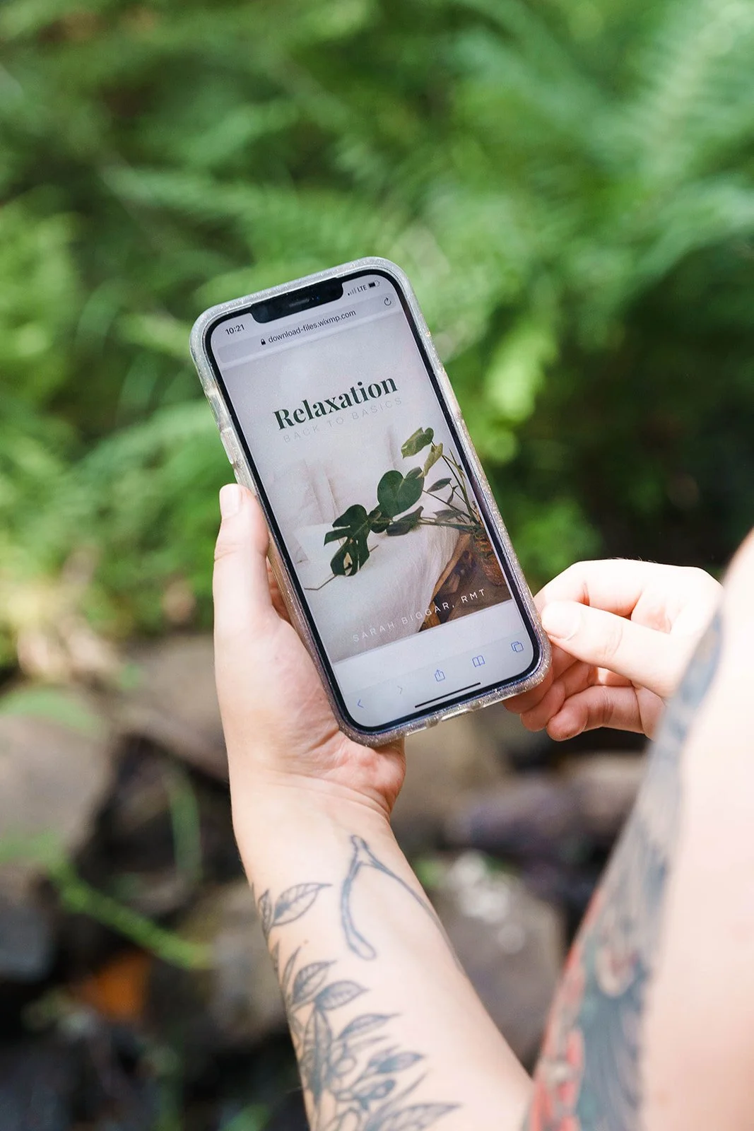 Person holding a smartphone with a 'Relaxation Back to Basics' webpage open, surrounded by greenery.