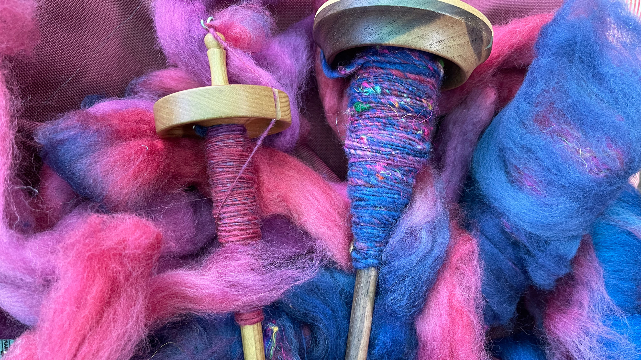 Two small spinning wheels with colorful yarn and felted wool in pink, purple, and blue hues.