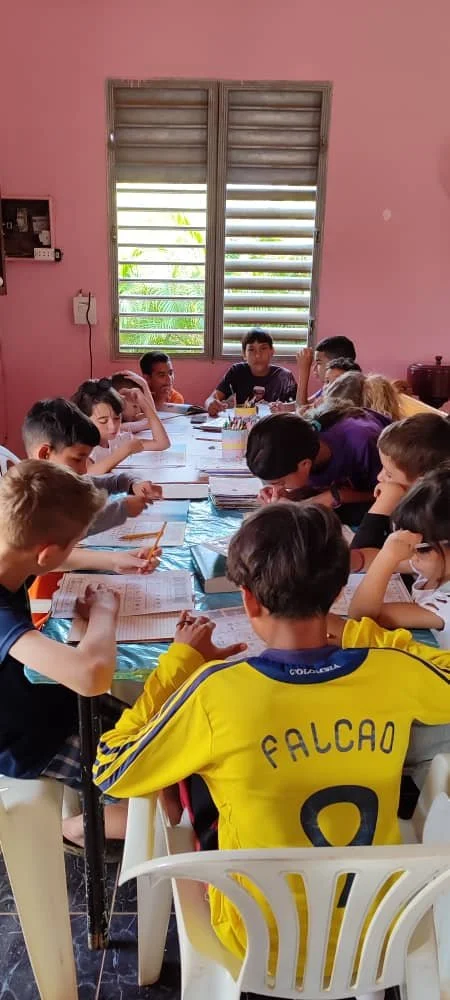 Classroom with children studying around a table, with pink walls and a window showing greenery outside, located in Matanzas, Cuba.