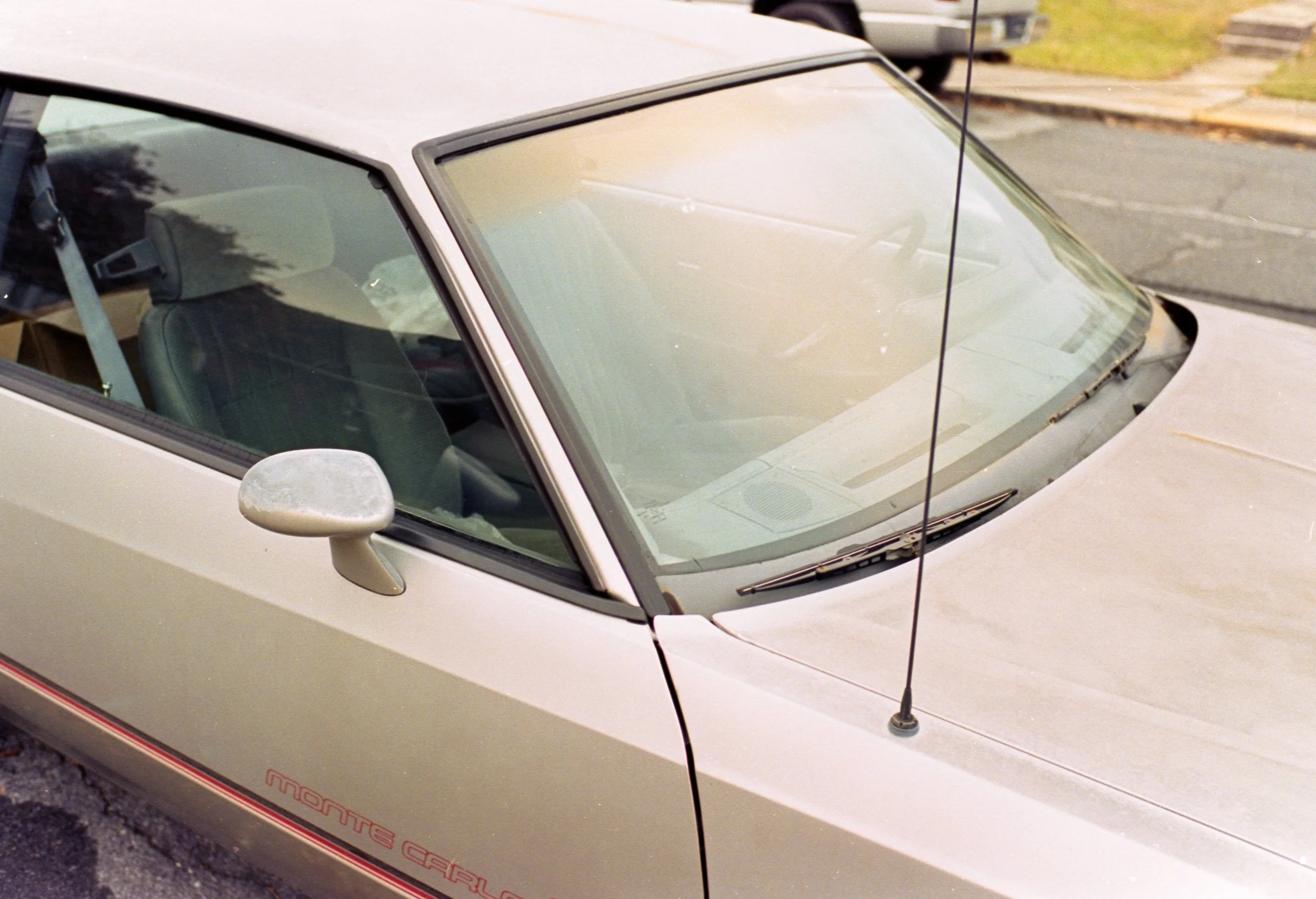 Close-up of a white vintage convertible car parked on a street, showcasing the windshield, side mirror, and part of the hood.
