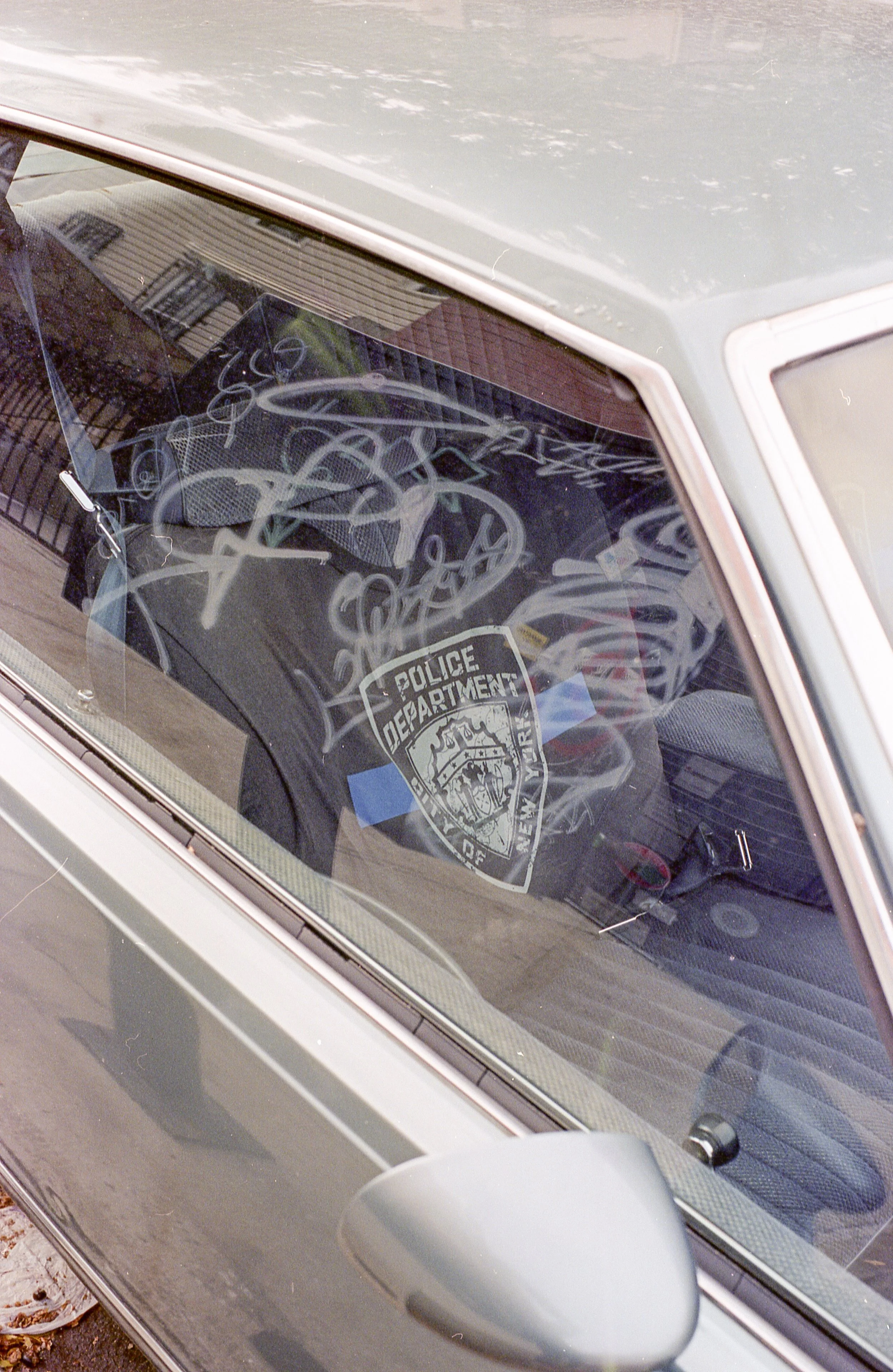 Front windshield of a gray police car with a 'Police Department' badge sticker and graffiti on the inside window.