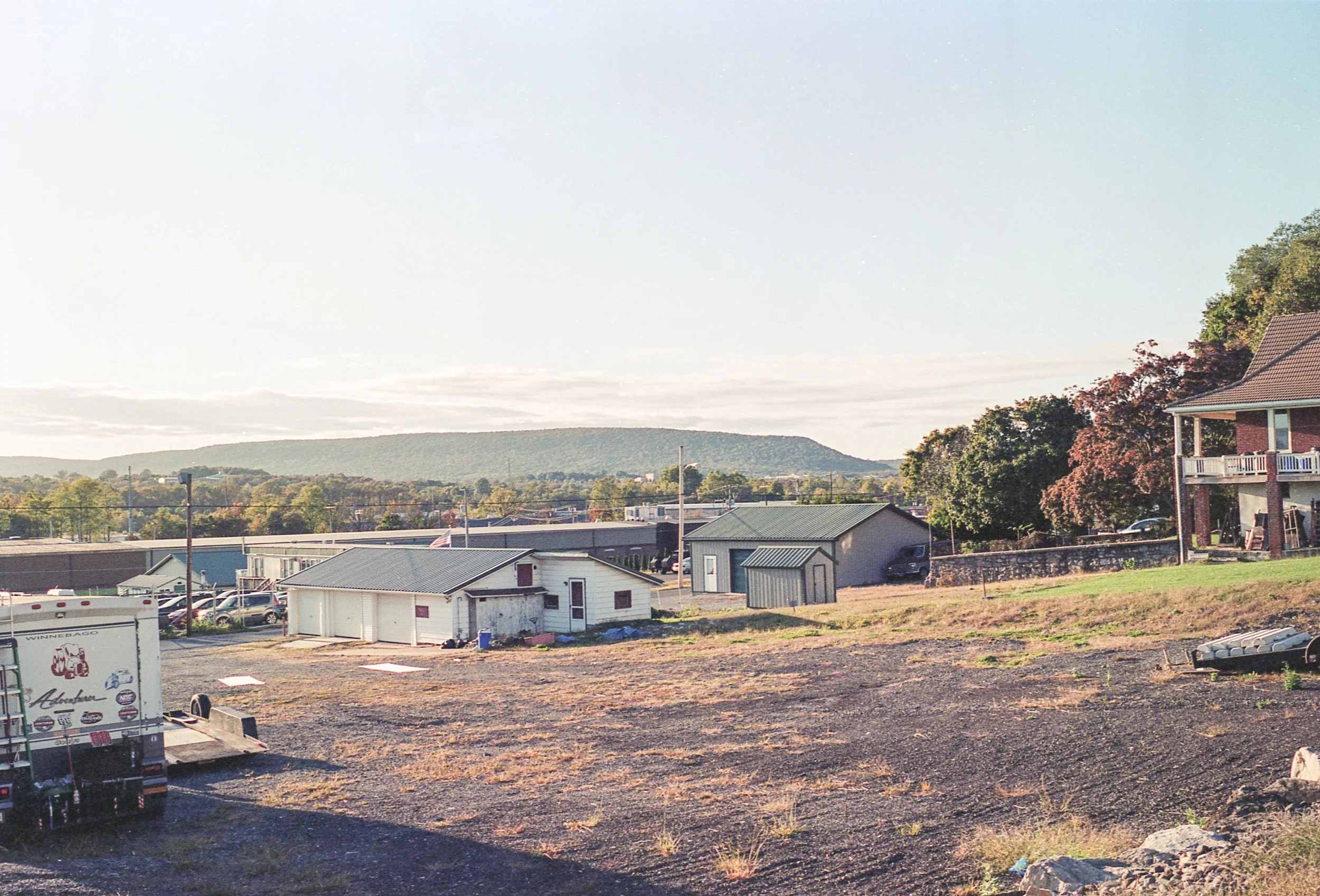 A small residential neighborhood with houses, trees, and a mountain in the background under a pale sky.